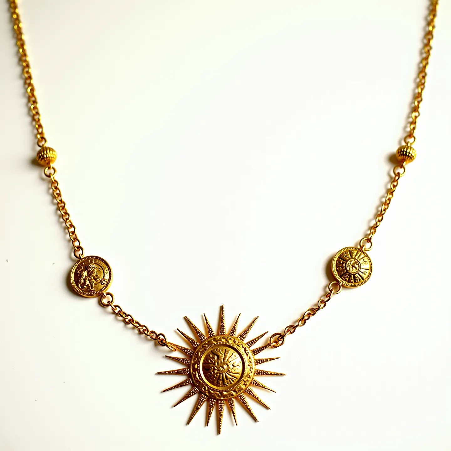 This long gold necklace features a series of intricately designed circular medallions with embossed patterns connected by delicate gold links. The centerpiece is a striking medallion, designed with a sunburst motif, radiating elegance and capturing attention with its unique texture. Smaller, complementary medallions are spaced along the chain, adding balance and continuity to the overall design. These medallions and the chain itself are crafted from a polished gold material, giving the necklace a luxurious and cohesive look. The necklace is composed of stylish, decorative elements but does not appear to contain additional gems or stones. The clasp or attachment design is not visible, focusing attention on the ornamental medallions that define the necklace's aesthetic.