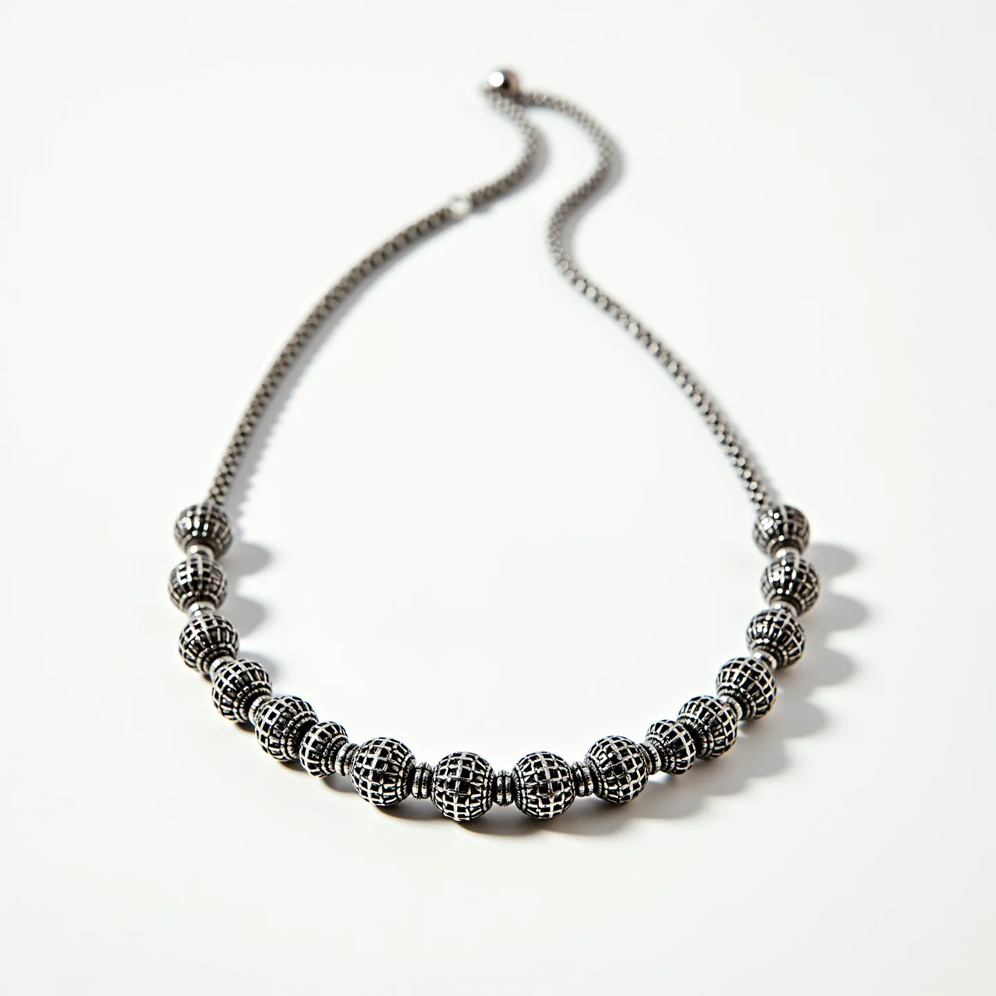 This men's beaded necklace features intricately designed beads made of metal, likely silver or silver-toned, each with a lattice pattern that adds texture and dimension. The beads are spherical and arranged in a symmetrical pattern, contributing to a balanced aesthetic. There is no visible use of gems or stones integrated into the design, maintaining a uniform metallic look. The clasp is a simple ball and hook, serving as a secure and seamless way to fasten the necklace. The overall design combines elegance with a slightly edgy, modern appeal, making it suitable for various occasions.