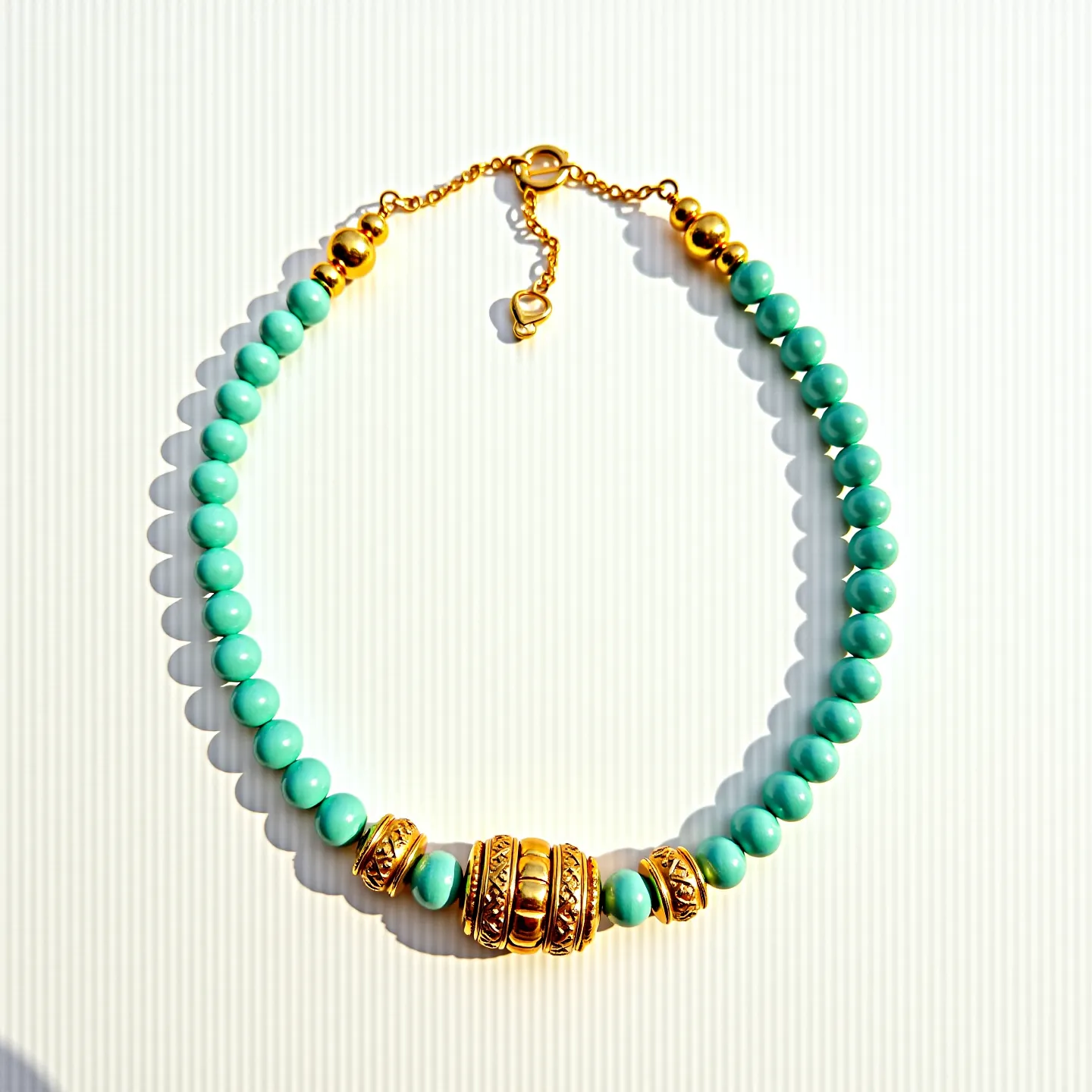 These men's beaded necklace features smooth, round turquoise-colored beads that are consistently sized and evenly strung. Positioned centrally, intricately detailed gold-tone spacer beads exhibit textured designs, adding contrast and elegance to the piece. The necklace secures with a gold-tone lobster clasp attachment, accompanied by an adjustable chain, allowing for flexibility in length and ease of use. The combination of vibrant turquoise and the warm gold-tone accents results in a striking, sophisticated appearance ideal for various styles.