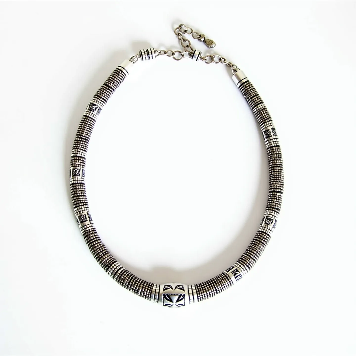 This men's beaded necklace features intricate patterns of small metal beads, likely made from stainless steel or a similar alloy, creating a textured appearance. Interspersed among these are decorative cylindrical and spherical beads with etched tribal-inspired designs. The necklace is secured with a metal lobster clasp, complete with an adjustable chain, providing versatility in length. The smooth and polished finish of the metal elements enhances its bold and masculine appeal, making it a statement piece for various styles and occasions.