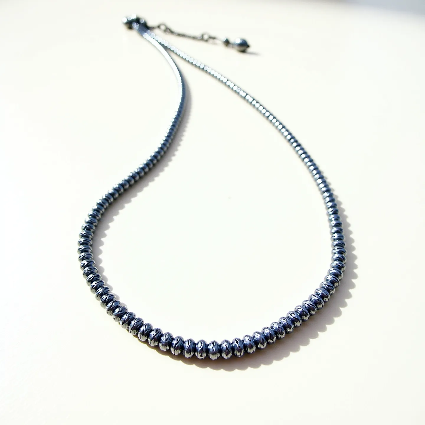 This men's beaded necklace features a series of metallic beads that are uniformly sized, creating a sleek and polished appearance. The beads are likely made of hematite, given their reflective dark gray finish, which provides a distinctive and contemporary look. The necklace includes a lobster clasp for secure attachment, and an extension chain allows for adjustable length, adding to its versatility. The overall design is minimalistic yet modern, making it a stylish accessory for various occasions.