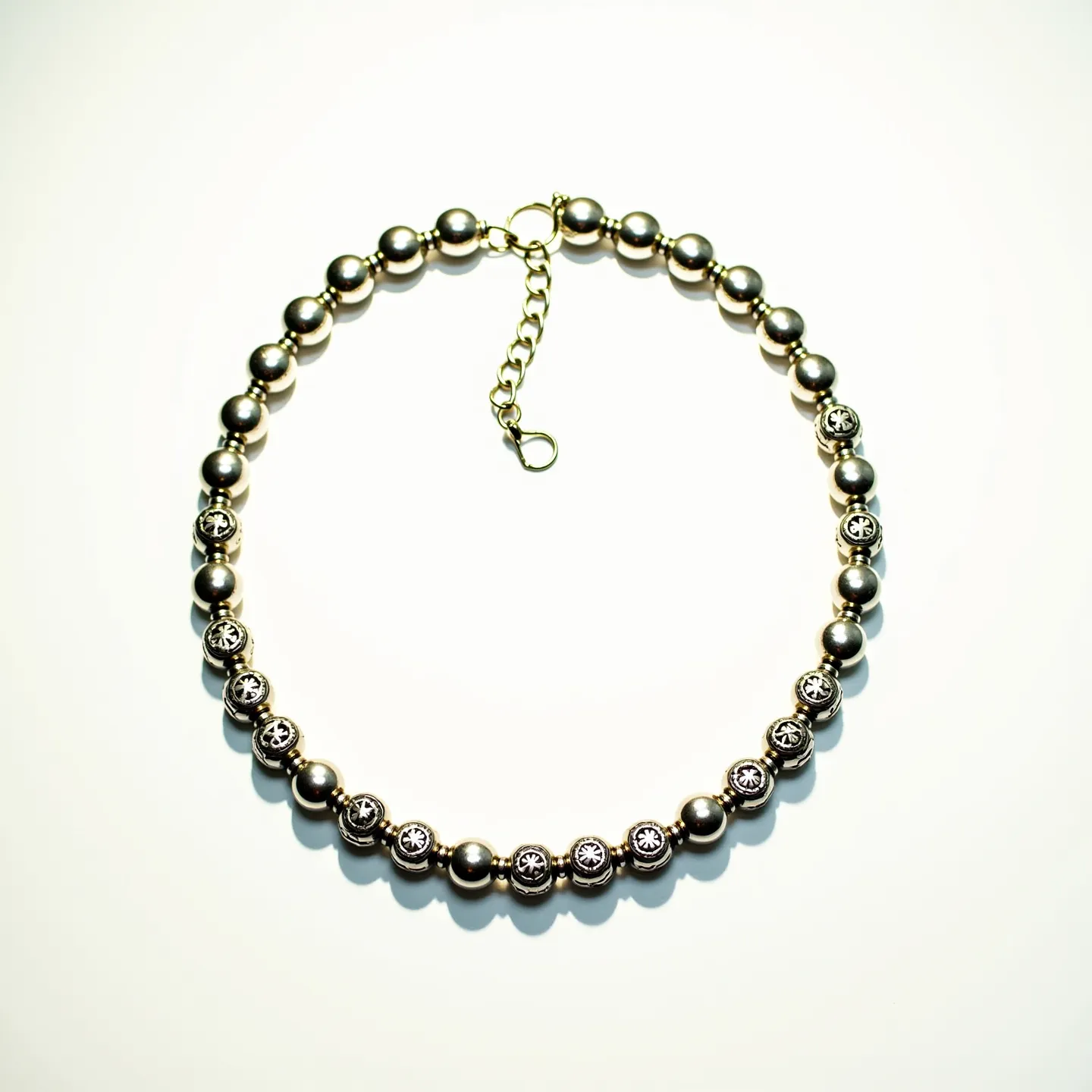 This men's beaded necklace features a combination of smooth, metallic beads and intricately decorated beads, possibly inset with small, round gemstones set in a decorative metal setting. The beads appear to be spaced evenly and are threaded securely. The necklace is fastened with a gold-toned chain clasp that includes an adjustable extension, allowing for flexibility in length. The design combines a modern metallic finish with classic elements, creating a versatile and stylish accessory.