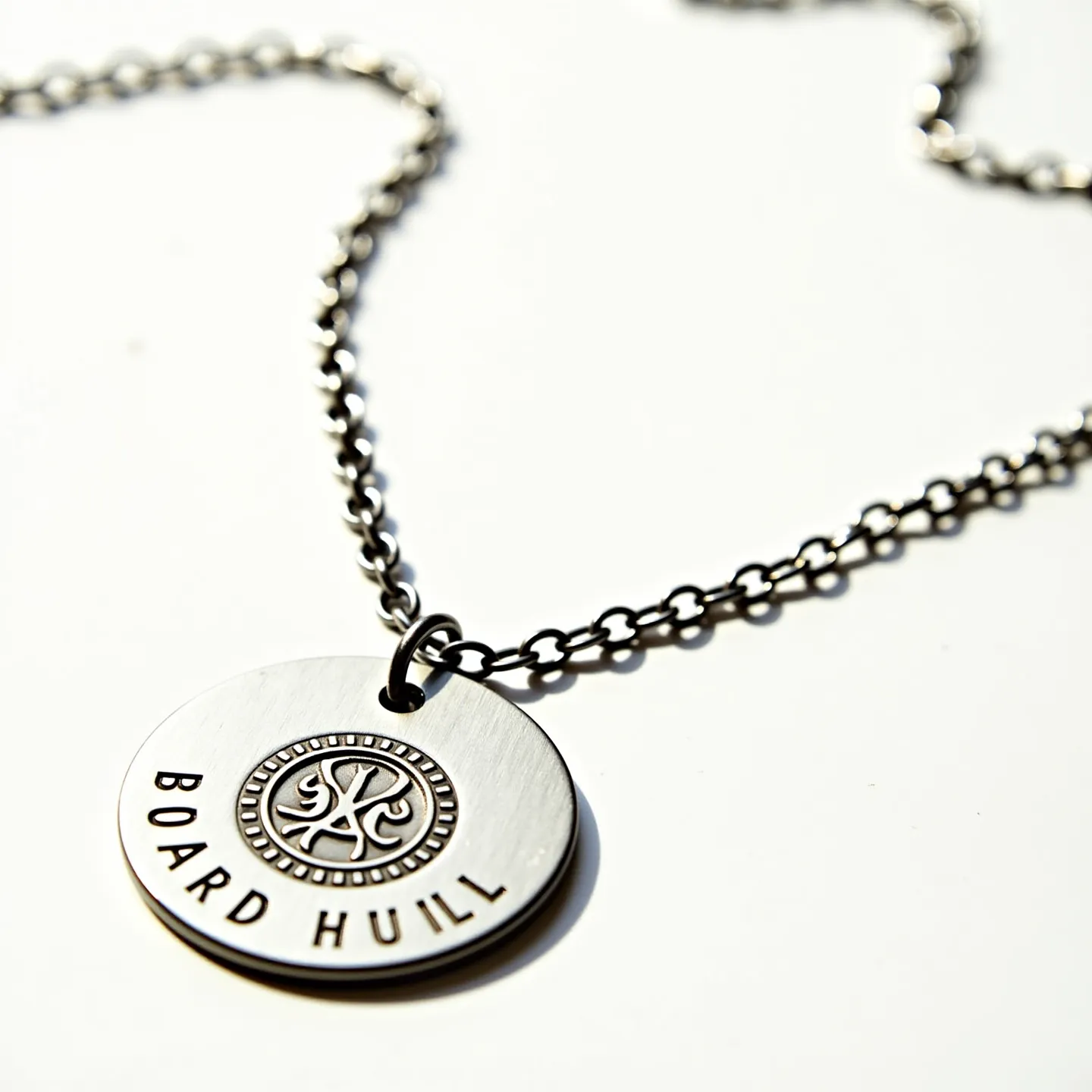 This men's necklace features a robust chain composed of linked metal, likely steel or another durable alloy, providing a sturdy and masculine appearance. The centerpiece is a round metal pendant, which is engraved with intricate detailing that includes a circular pattern and the text "BOARD HULL." The pendant is attached to the chain through a simple metal loop, ensuring it hangs securely. There are no visible gems or stones incorporated into the design, and a typical clasp or attachment likely used for necklace closures can be assumed to provide easy wearability. Overall, the piece exhibits a combination of industrial and personalized elements suitable for everyday wear.