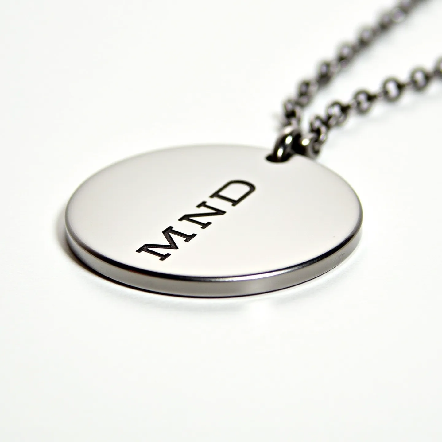 This men's necklace features a sleek, round metallic pendant engraved with the letters "MND." The pendant is polished to a high shine, giving it a modern and sophisticated look. It hangs from a durable chain that appears to be made of a similar metal, possibly stainless steel, providing both a stylish and sturdy appearance. The chain is constructed of uniformly linked loops that complement the minimalist design of the pendant. A classic clasp ensures secure wearability, blending seamlessly with the overall aesthetic of the necklace.