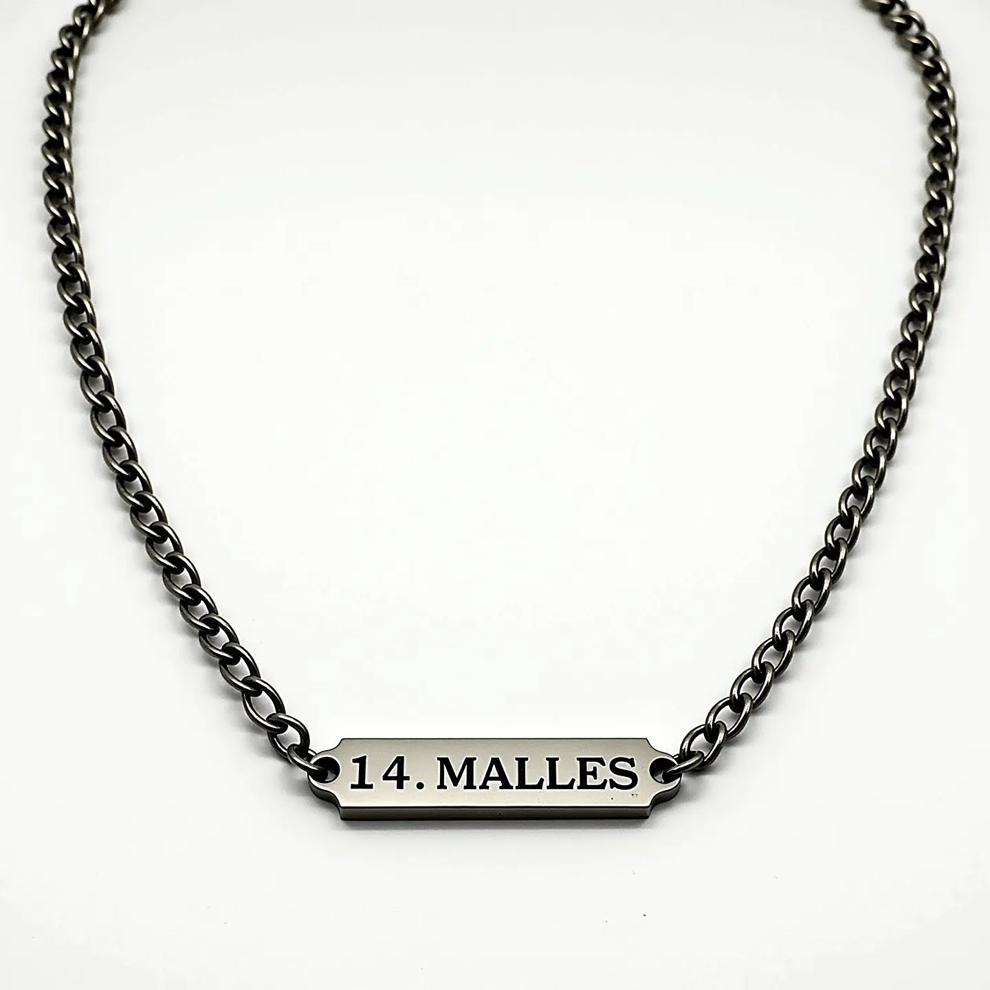 This men's necklace features a robust chain likely made from stainless steel, giving it a sleek, polished look. The central element is a rectangular metal plate, engraved with "14. MALLES," suspended between the links. The chain is composed of evenly sized interlocking loops, designed to ensure durability and a stylish appearance. The necklace is equipped with a classic lobster clasp, providing secure closure while allowing for easy removal and adjustment. Its minimalist yet bold design makes it a versatile accessory.