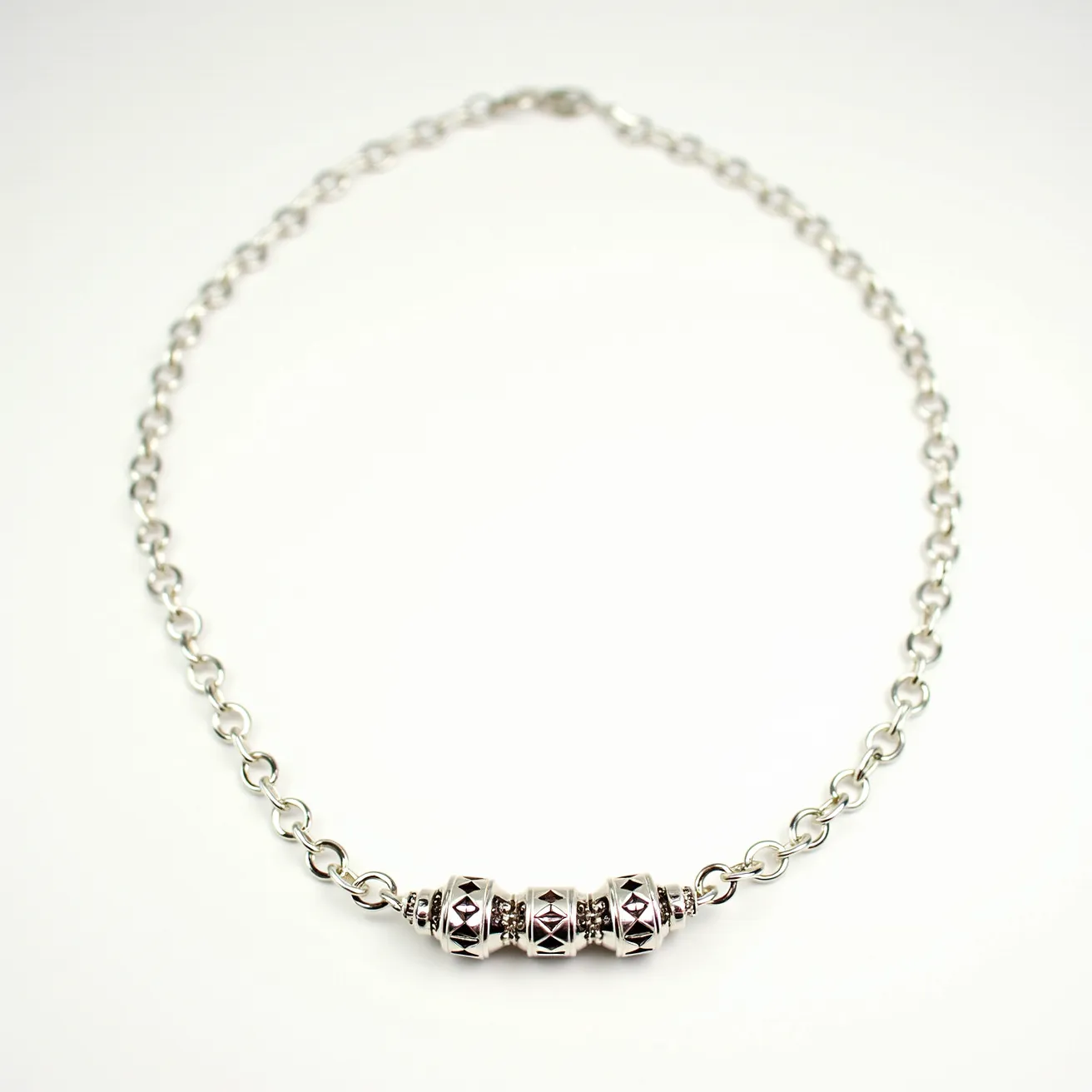 This men's necklace features a series of interconnected metal links, likely crafted from stainless steel or a similar durable metal, giving it a sleek and modern appearance. At the center of the design are three ornamental beads, each adorned with geometric patterns that add a touch of intricate craftsmanship. These beads are cylindrical with a faceted design but do not appear to contain any gemstones. The necklace is secured with a conventional clasp, ensuring both functionality and style.