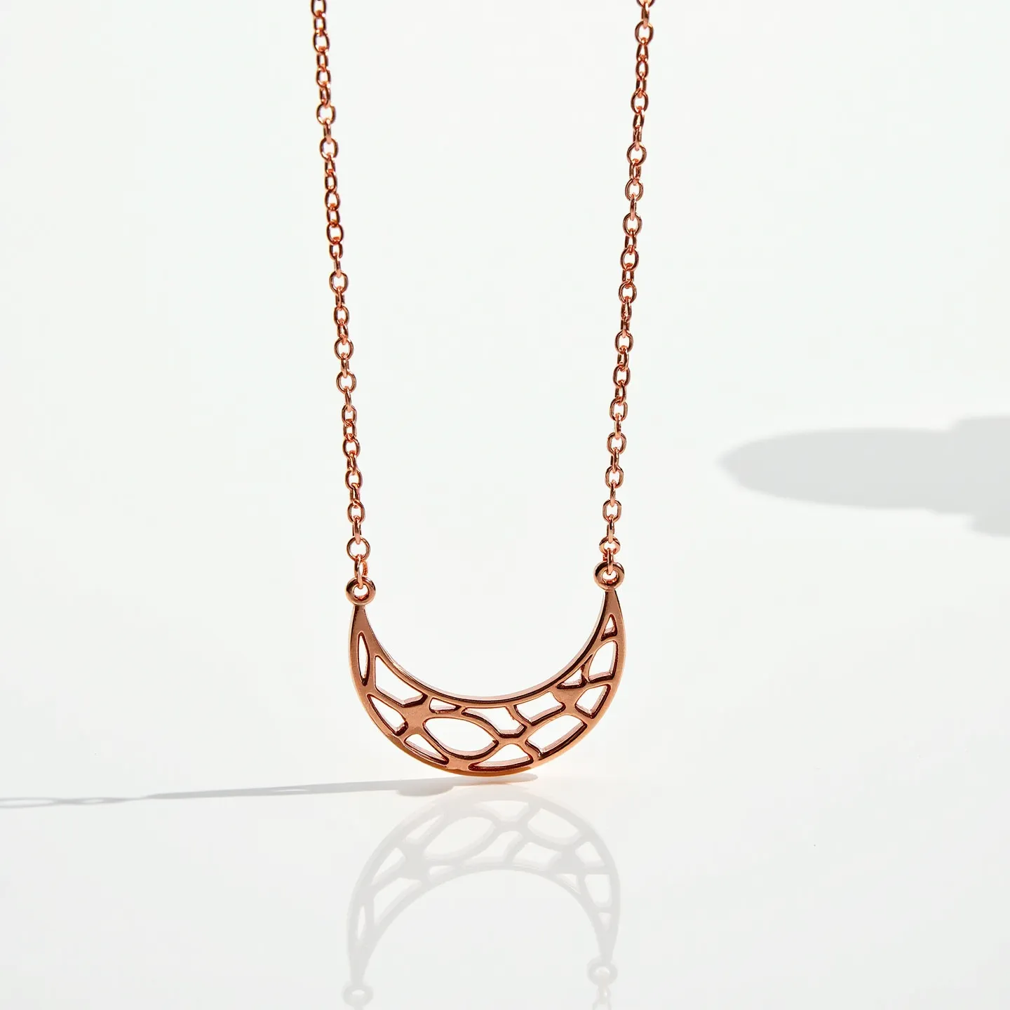 This celestial moon necklace features a crescent-shaped pendant crafted from a warm-toned metal, likely rose gold or a similar hue, with an openwork design that adds an airy elegance. The pendant is suspended from a matching chain composed of delicate links, allowing the necklace to rest comfortably on the wearer. The intricate pattern within the crescent reflects a modern, minimalist aesthetic, enhancing its celestial theme. The necklace secures with a small yet sturdy clasp that complements the overall design, ensuring both style and functionality for everyday wear.