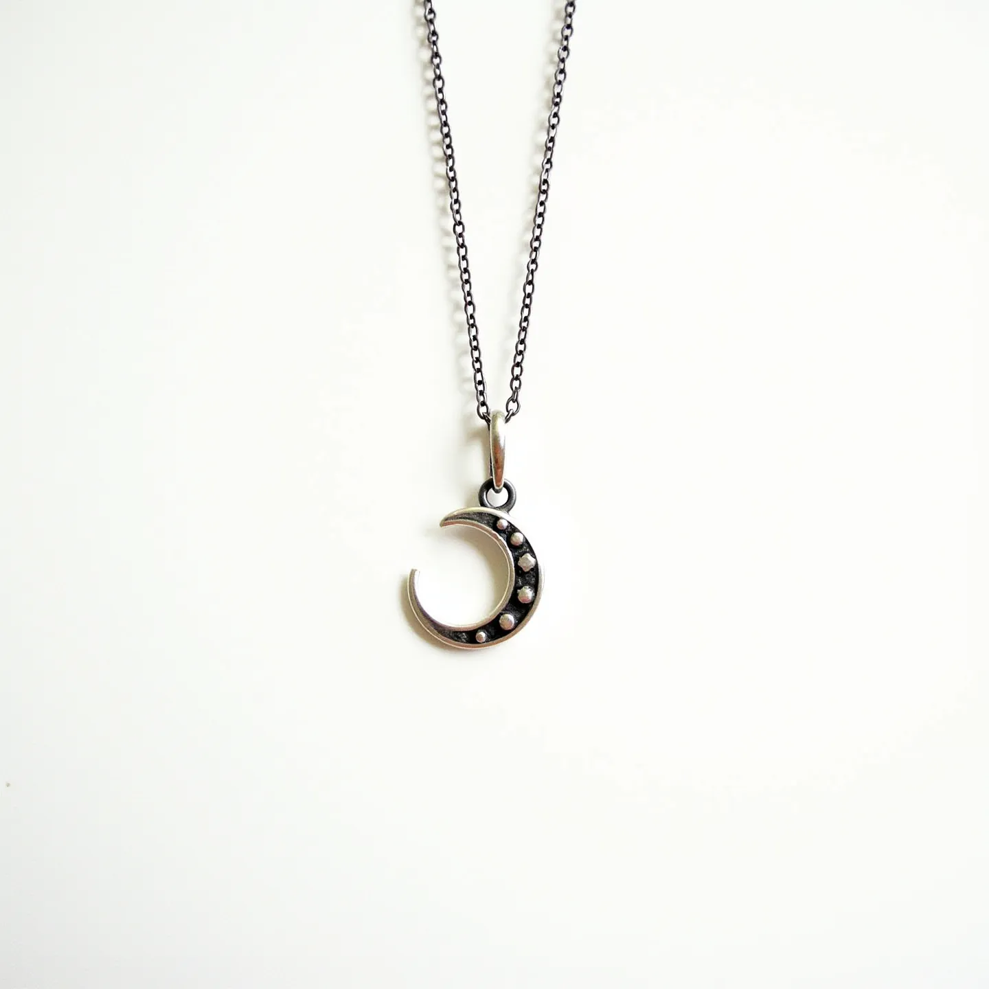 This celestial moon necklace features a delicate crescent moon pendant made of a metal with a dark, oxidized finish, suggesting materials such as sterling silver. The crescent is adorned with black stones set in a small circular setting along its inner curve, enhancing its celestial theme. The pendant is suspended from a fine link chain, which complements the pendant with its subtle yet elegant appearance. The necklace is equipped with a simple yet functional clasp, ensuring ease of wear and a secure fit.