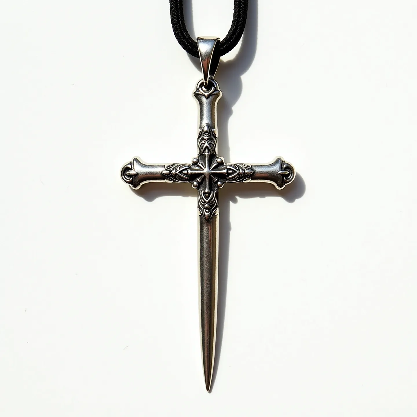 This nail cross necklace features a detailed design made of a silver-toned metal, shaped to resemble two intertwined nails forming a cross. The surface of the cross displays intricate engravings, emphasizing medieval-style motifs at the intersections and ends of the nails. The pendant is suspended from a black, braided cord, visible through a metal loop at the top of the cross, which secures the necklace and adds to its rugged aesthetic. The craftsmanship highlights a blend of simplicity and elegance, creating a striking piece of jewelry with symbolic meaning.