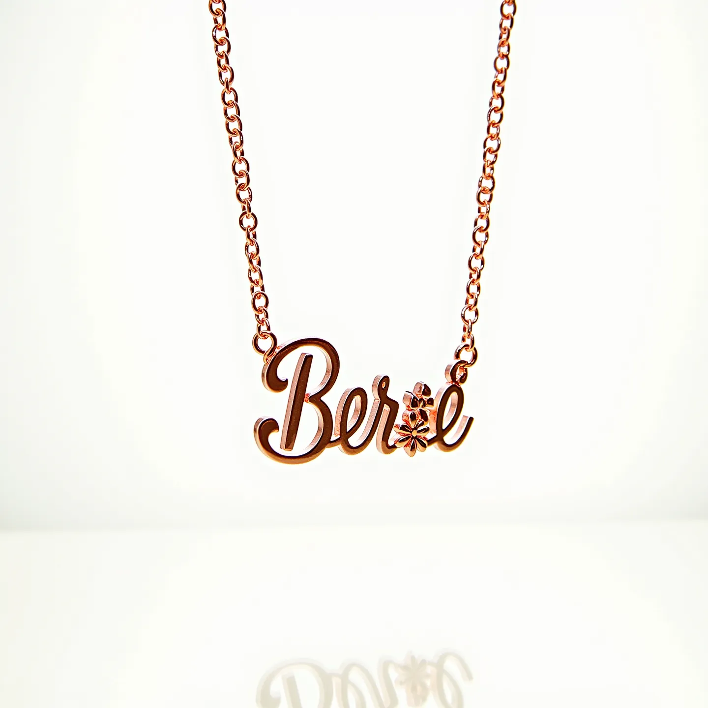 This name chain necklace features the name "Bere" in a stylized script, crafted from a rose gold-toned metal. The necklace includes a dainty flower detail adorning the name, which appears to be complemented by a small, clear gemstone set into the center of the flower. The chain is a simple link chain, providing an elegant and seamless connection to the nameplate. The necklace is secured with a standard lobster clasp, ensuring both durability and ease of use.