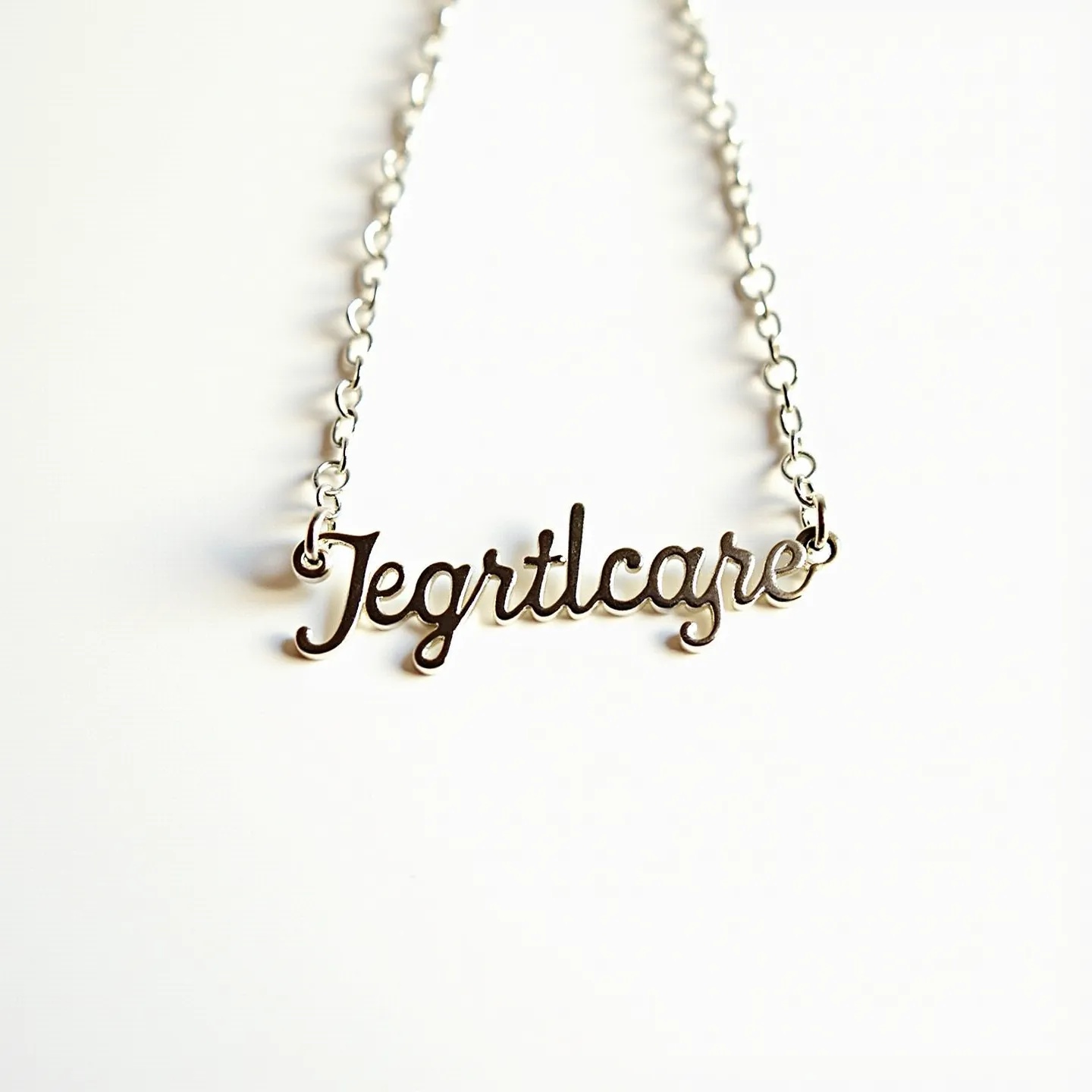 This name chain necklace features a delicate and polished metallic chain, seamlessly integrated into a script-style pendant that spells out the word. The pendant connects to the chain at both ends, suggesting a sturdy and durable design. The chain itself consists of interlinked oval links, exuding a refined and minimalist aesthetic. The necklace does not display any gems or stones, focusing on the simplicity and elegance of the metallic form. It includes a classic spring ring clasp, contributing to secure wearability while enhancing the necklace's understated elegance.