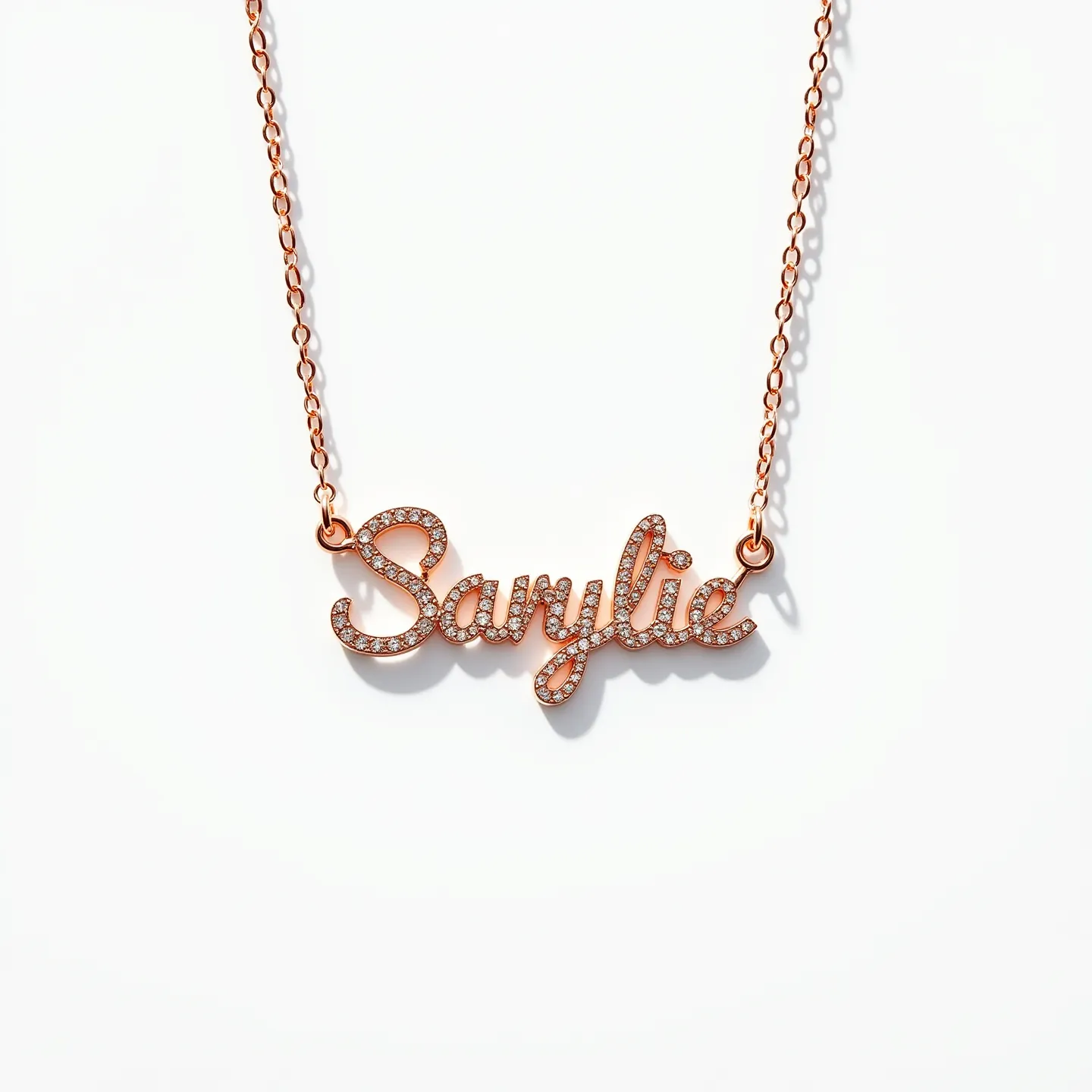 This name necklace features elegant script spelling out the name, crafted from a rose gold metal. The letters are adorned with small, round-cut diamonds that are pave-set, adding a sparkling effect to the intricate design. The necklace is attached to a delicate rose gold chain, which includes small circular links that connect to the nameplate on both ends. The overall design showcases a harmonious blend of luxury and personalization, making it a beautiful accessory.