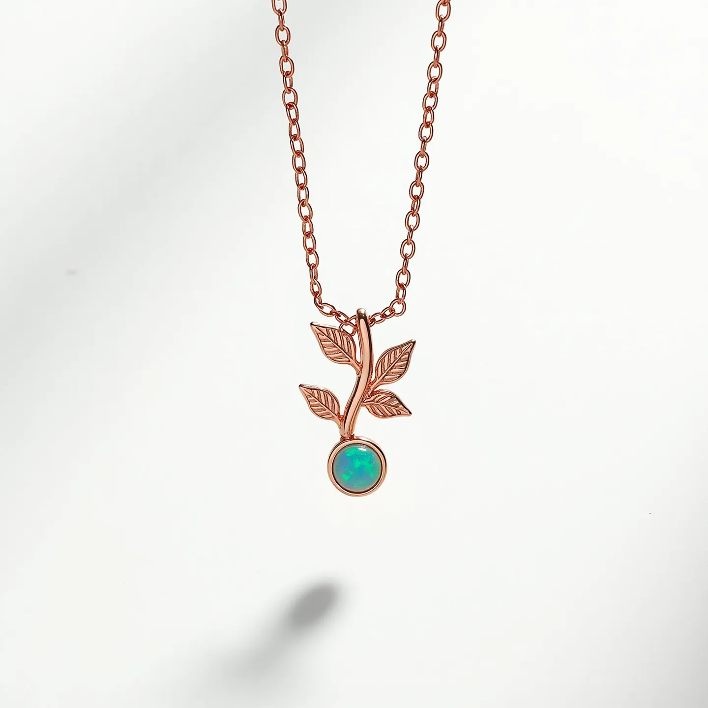 This opal necklace features a delicate chain made of a rose gold-toned metal, elegantly showcasing a pendant in the shape of a branch with two intricately detailed leaves. The centerpiece of the pendant is a round, cabochon-cut opal, displaying a vibrant play of colors typical of opals. The stone is secured in a bezel setting, which provides a smooth and modern look while ensuring the opal is held securely. The style and materials give the necklace a harmonious blend of natural inspiration and refined craftsmanship.