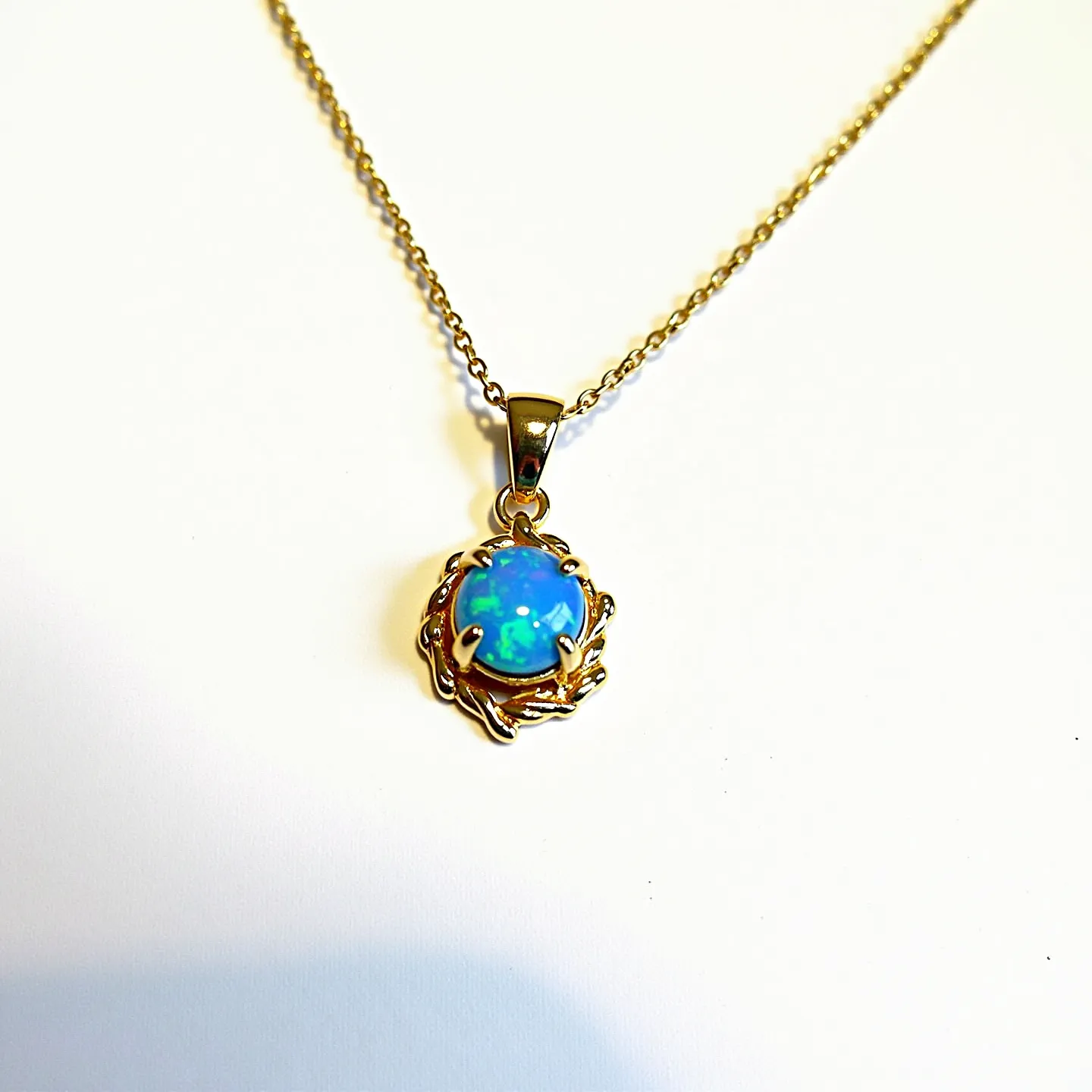 This opal necklace features a vibrant, round opal gemstone with a mesmerizing play of colors, predominantly blue and green, set in a decorative gold setting. The gold setting is crafted in a swirl design that elegantly frames the opal, adding a touch of sophistication. The chain is a fine gold link, complementing the overall design with its simple elegance. The pendant is attached via a sleek, polished gold bail that matches the color and style of the chain. The combination of the opal's vivid colors and the warm gold tones creates a strikingly beautiful piece of jewelry.