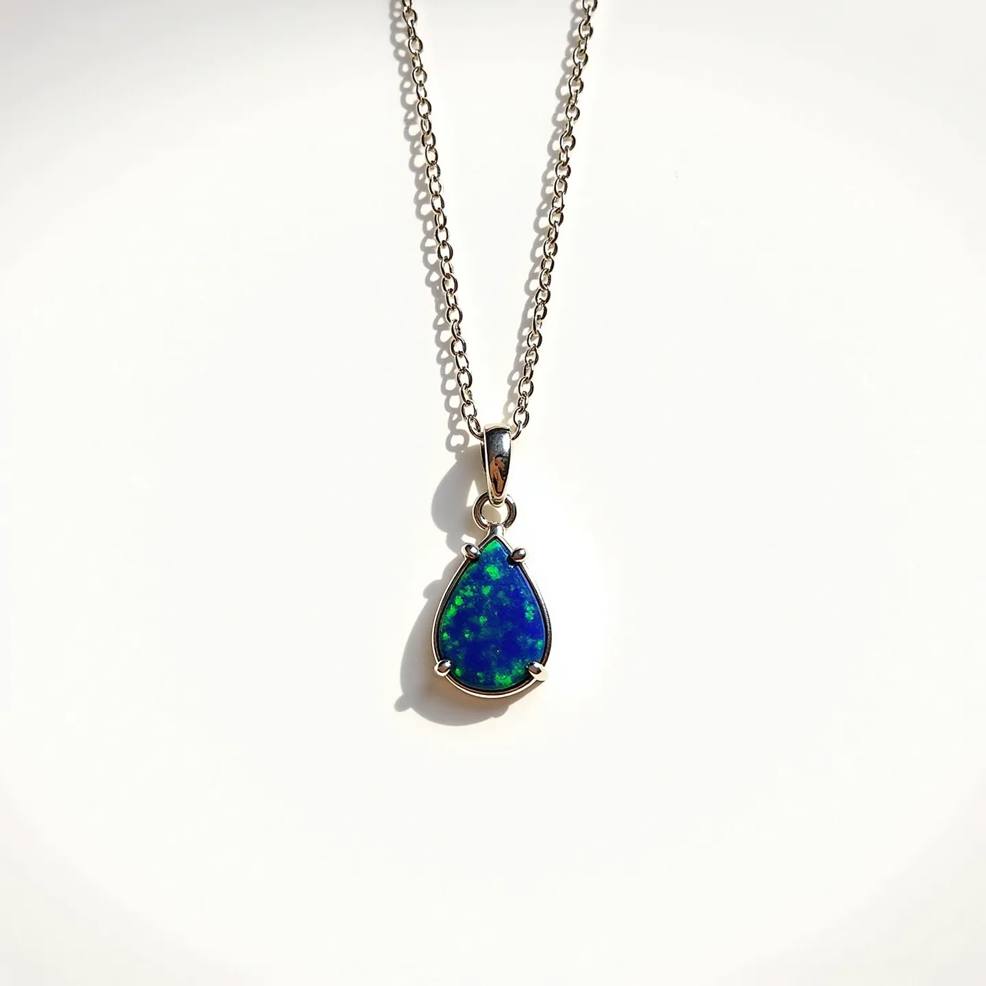 This opal necklace features a striking teardrop-shaped opal gemstone with vibrant blue and green hues that catch the light beautifully. The opal is set in a polished metal bezel, likely silver, which provides a sleek and elegant frame for the stone. The chain is a delicate, fine-link style that complements the pendant's sophisticated appearance. The necklace is finished with a simple and functional clasp, ensuring it can be worn securely. The design emphasizes the opal's natural beauty while maintaining a classic and timeless aesthetic.