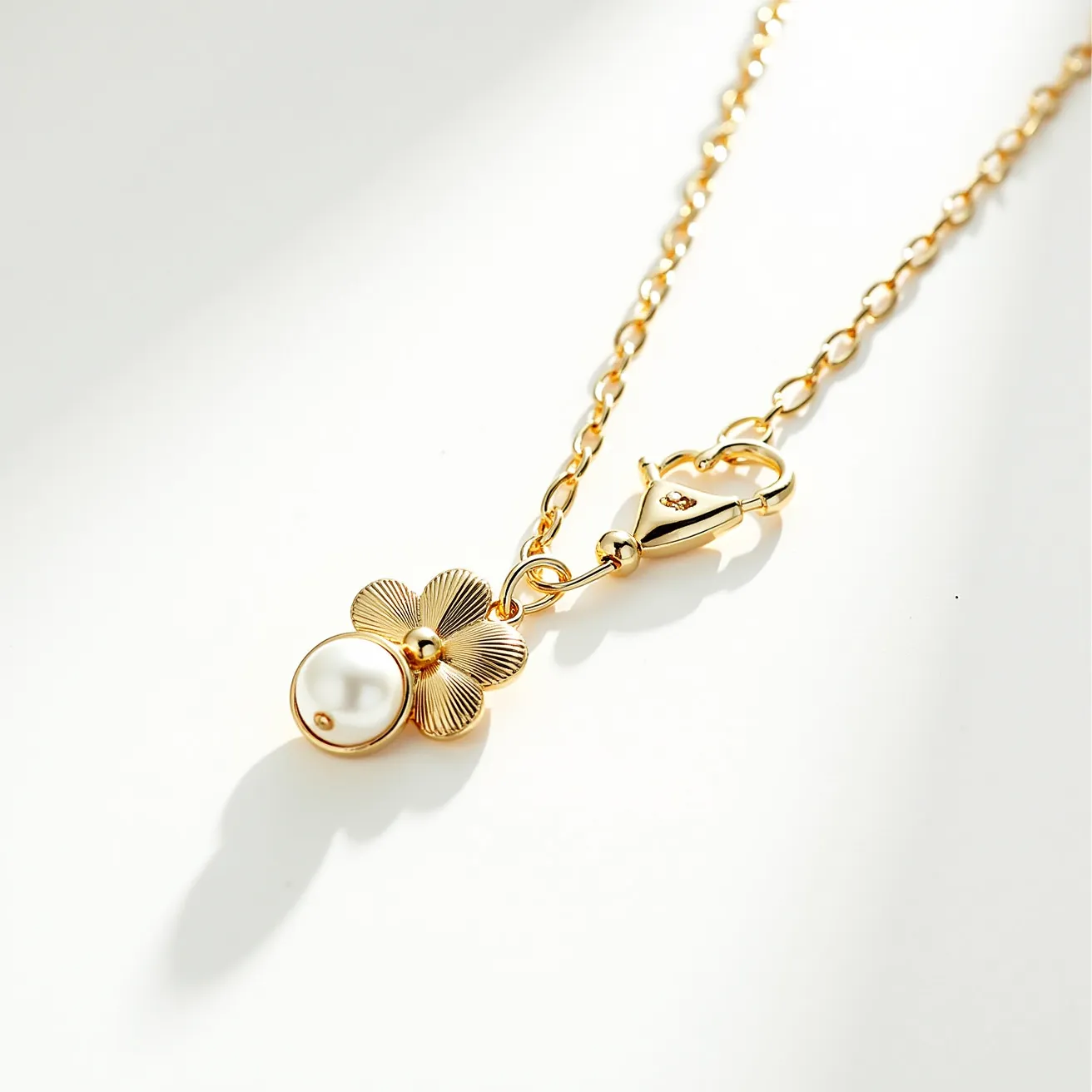 This pearl necklace features a delicate pearl set in a floral motif crafted from gold-toned metal. The pearl is positioned within a gold bezel setting, enhancing its luster and elegance. The chain is composed of linked gold-toned segments, culminating in a lobster claw clasp that ensures secure wear. The floral design provides an artistic touch, with intricately textured petals accentuating the pearl's natural beauty.