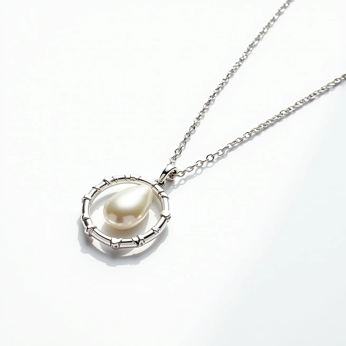 This pearl necklace features a distinctive design with a teardrop-shaped pearl as the central gem. The pearl is elegantly suspended within a circular pendant, crafted with a textured pattern that resembles bamboo or a similar organic motif. The setting is likely made of a silver or white gold metal, lending a sleek, polished look to the piece. The necklace chain is composed of delicate links, complementing the size of the pendant and ensuring a refined, elegant appearance. The clasp appears to be a traditional style, designed for both security and ease of use.