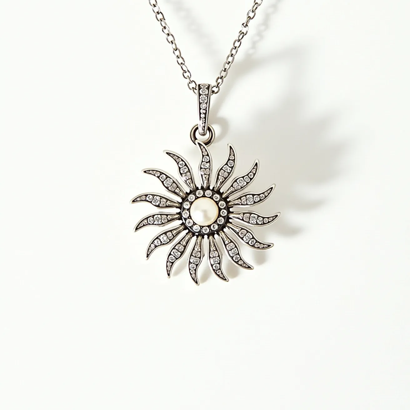 This pearl necklace features a striking pendant design. At the center, there is a round pearl surrounded by a sunburst pattern, with tendrils extending outward. These tendrils are adorned with small, clear stones that appear to be diamonds, each set in open prong settings to enhance their sparkle. The pendant is attached to a delicate chain, which complements its elegant design. The metal used for the chain and setting appears to be a polished silver or white gold, enhancing the overall luster of the piece. The clasp is not visible, but the design suggests a seamless and secure connection.