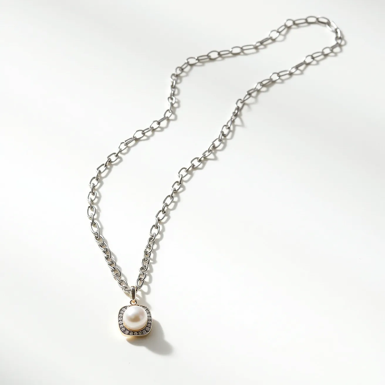 This pearl necklace features a single cream-colored pearl set in the center of a pendant. The pearl is encircled by a series of small, round gemstones, likely diamonds or cubic zirconia, in a subtle pavé setting, adding a touch of sparkle. The pendant is attached to a fine, silver-toned chain with interlocking links, which provide a contemporary and elegant design. The clasp, although not fully visible, appears to be a standard lobster clasp, providing secure closure. The overall design combines the timeless appeal of pearls with a modern twist, making it versatile for various occasions.