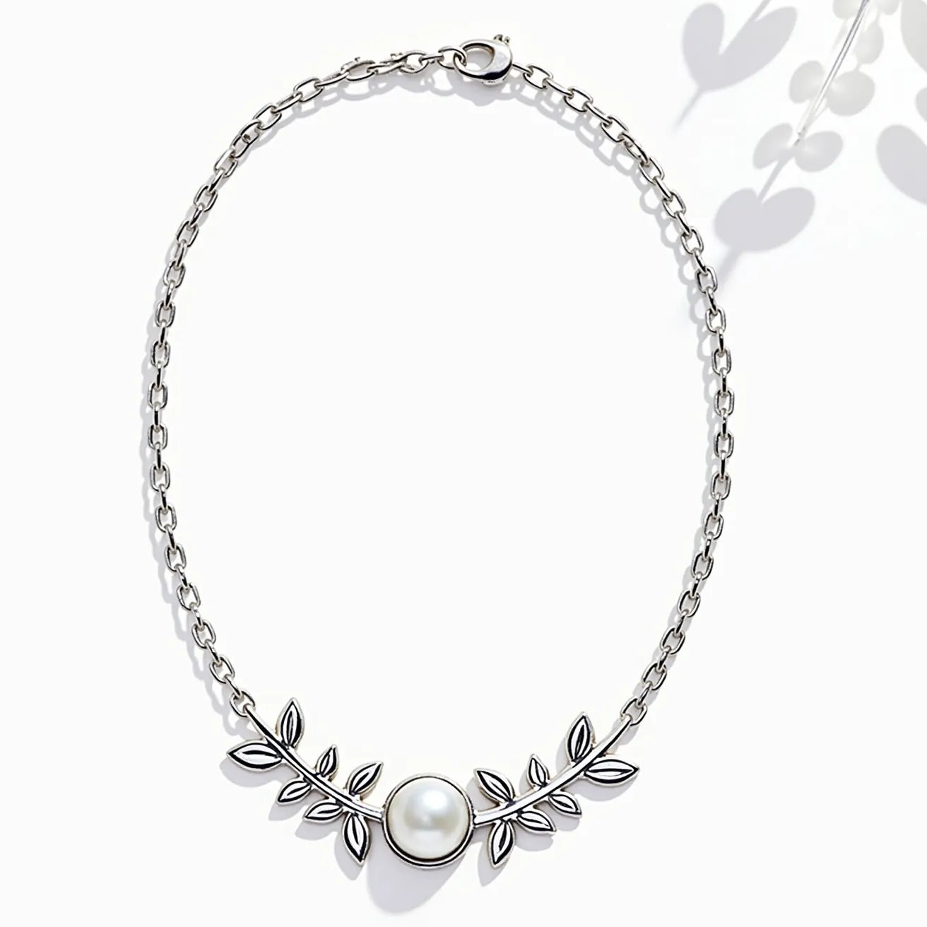 This pearl necklace features a central round pearl set within a graceful, vine-like metal setting adorned with leaf motifs. The chain is composed of interlinked metal loops, giving it a classic, elegant look. The pearl is smooth and luminous, suggesting a high-quality material that adds a touch of sophistication to the design. The necklace is secured with a lobster clasp, offering both functionality and a seamless appearance. The overall design is refined, blending the natural beauty of the pearl with a modern metalwork setting.