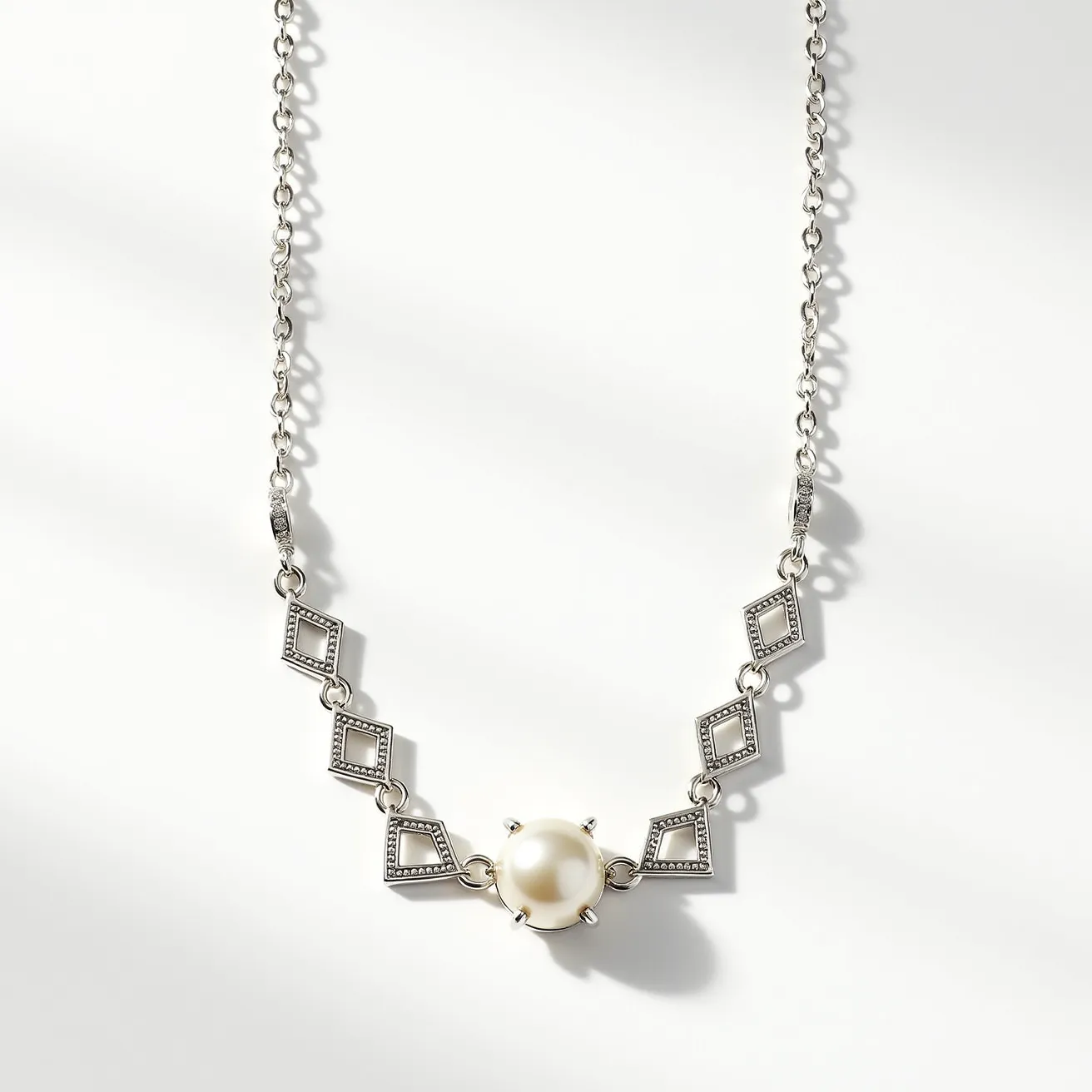 This pearl necklace features a central round pearl set in a metal prong setting, which showcases its glossy surface and lustrous sheen. The design is complemented by a series of diamond-shaped metal links, creating an elegant pattern that adds a modern touch to the classic pearl. The metal appears to be a shiny silver or white gold, enhancing the overall sophistication of the piece. The necklace is equipped with a chain that integrates seamlessly with the geometric motif, providing both style and function. The closure mechanism is a standard clasp, ensuring secure wear while maintaining the necklace's refined appearance.