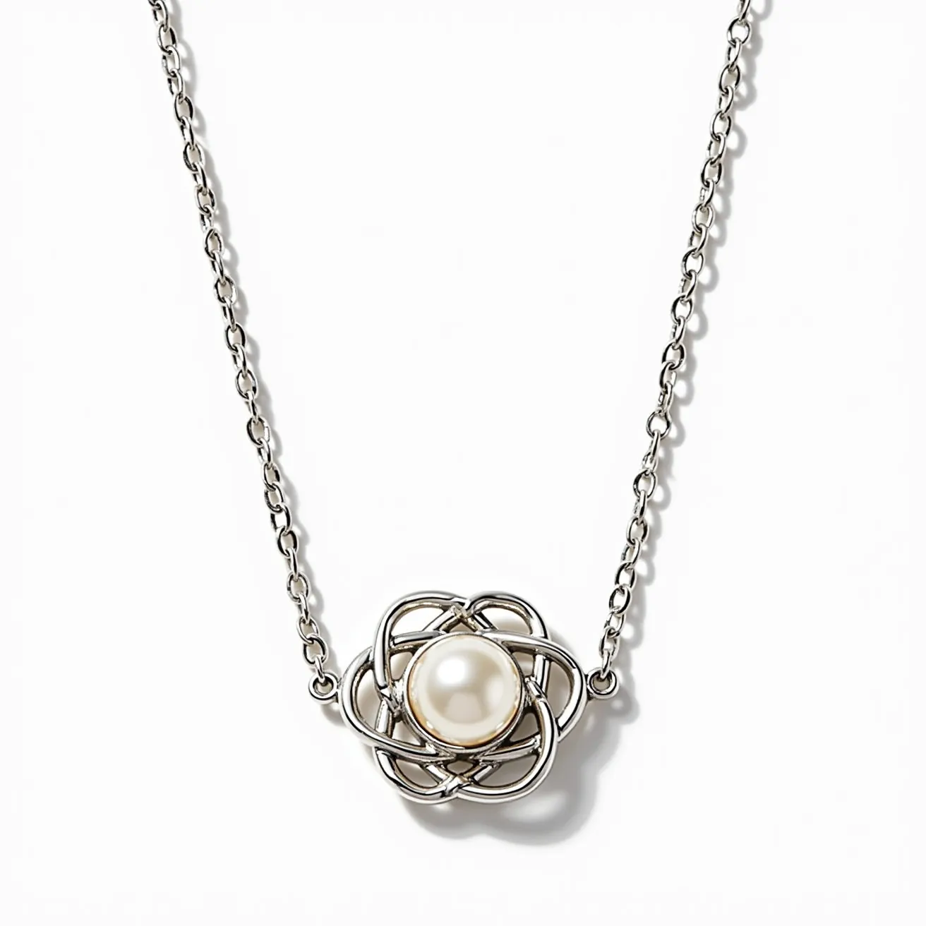 This pearl necklace features a single, round pearl set at the center of a delicate interwoven metal design that resembles a flower. The pearl appears to be of a lustrous white hue. The metal, possibly silver or white gold, forms a cage-like setting around the pearl, adding an intricate and elegant touch. The necklace is completed with a fine chain that maintains the overall dainty aesthetic. This design accentuates the natural beauty of the pearl while providing a modern twist with its unique setting.