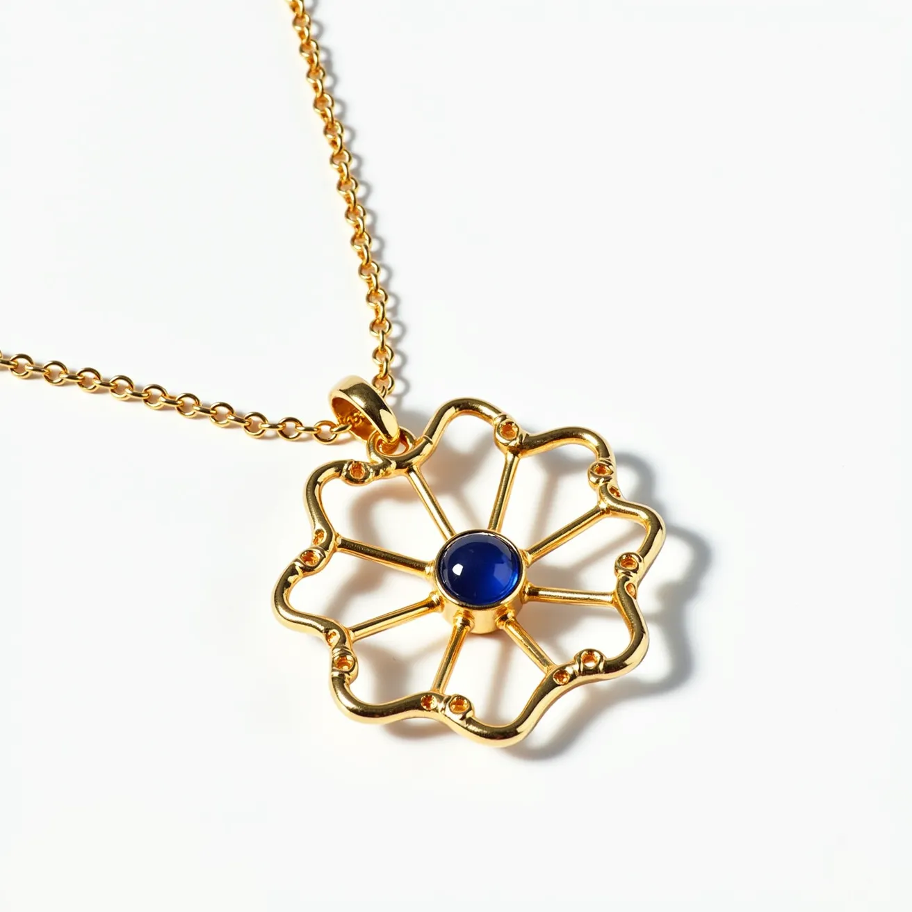 This statement pendant features a striking floral design crafted from what appears to be gold-tone metal. At its center is a deep blue cabochon gem, likely a sapphire, set in a bezel setting that enhances its rich color and smooth surface. The petal-like structure of the pendant is accentuated by intricate gold spokes extending from the center, giving the piece an elegant and airy feel. The pendant is suspended from a delicate link chain, which is attached using a polished gold bail, allowing the pendant to hang gracefully. The overall craftsmanship blends a modern aesthetic with classic elegance, making it a standout piece.