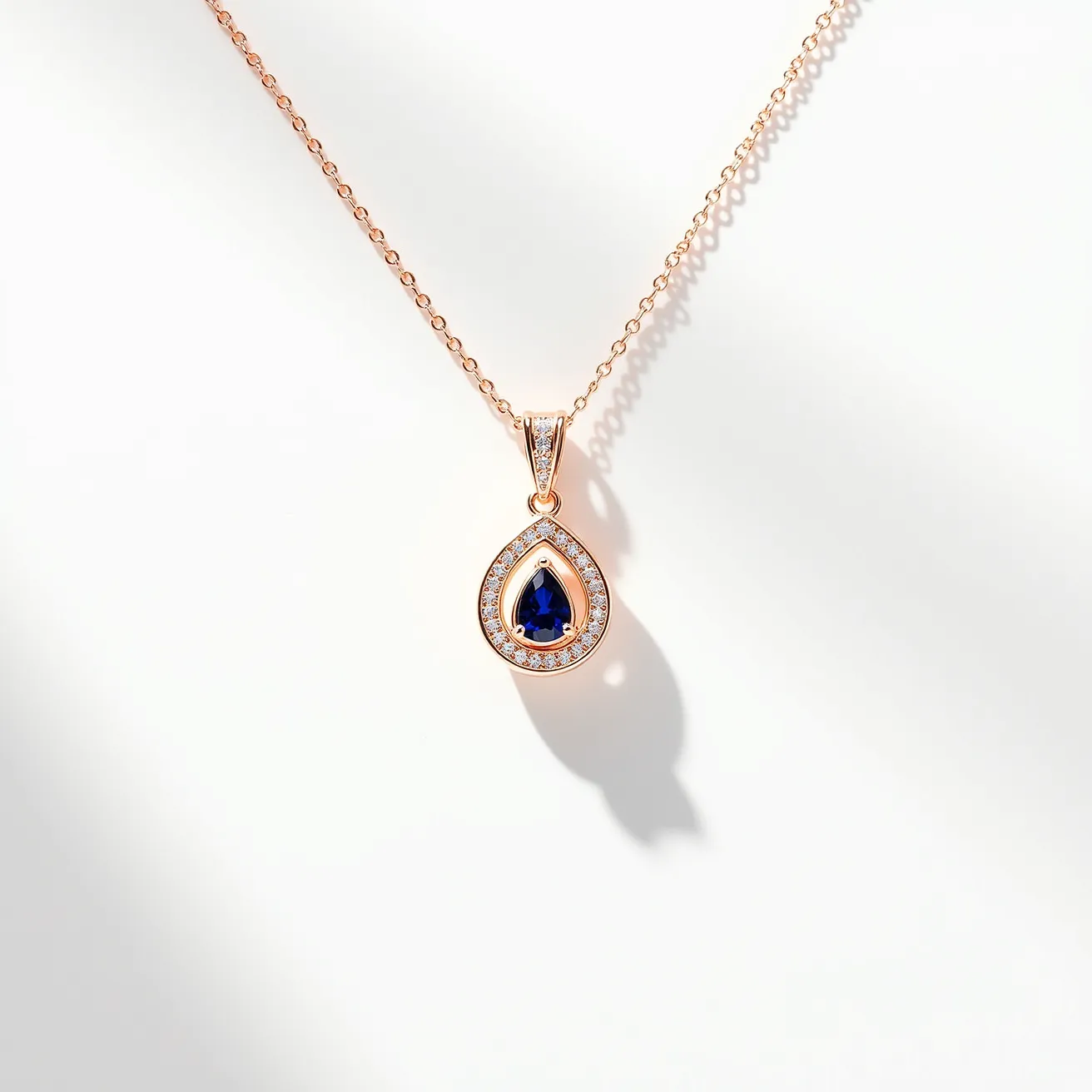 This statement pendant features a teardrop design with a central blue gemstone, likely a sapphire, cut in a teardrop shape. The central stone is set within a halo of small, round white gems, possibly diamonds, that accentuate its vibrant color. The setting is crafted from a warm-toned metal, possibly rose gold, which provides a striking contrast to the gemstones. The pendant is attached to a delicate chain with a complementary metal clasp, showcasing both elegance and functionality. The overall design is both classic and eye-catching, making it a sophisticated piece of jewelry.