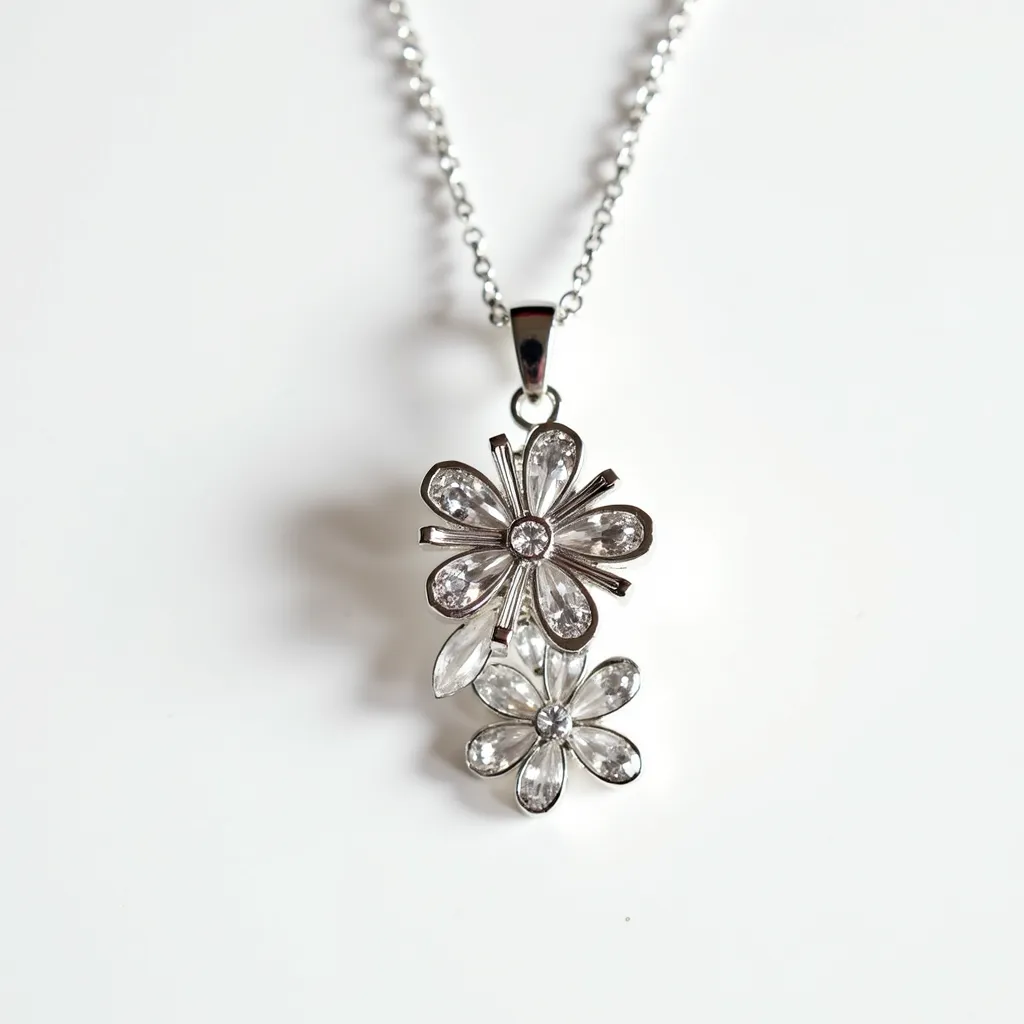 This statement pendant features two intricate floral designs, crafted from a shiny metal, likely silver or white gold, which forms the delicate petals of the flowers. Each flower is adorned with clear gemstones that resemble marquise and round cuts, secured in a bezel setting that highlights their brilliance and clarity. The pendant is attached to a simple yet elegant chain via a polished metal bail that complements the overall design. The craftsmanship emphasizes the elegance and sophistication of the floral motif, making it a striking accessory.