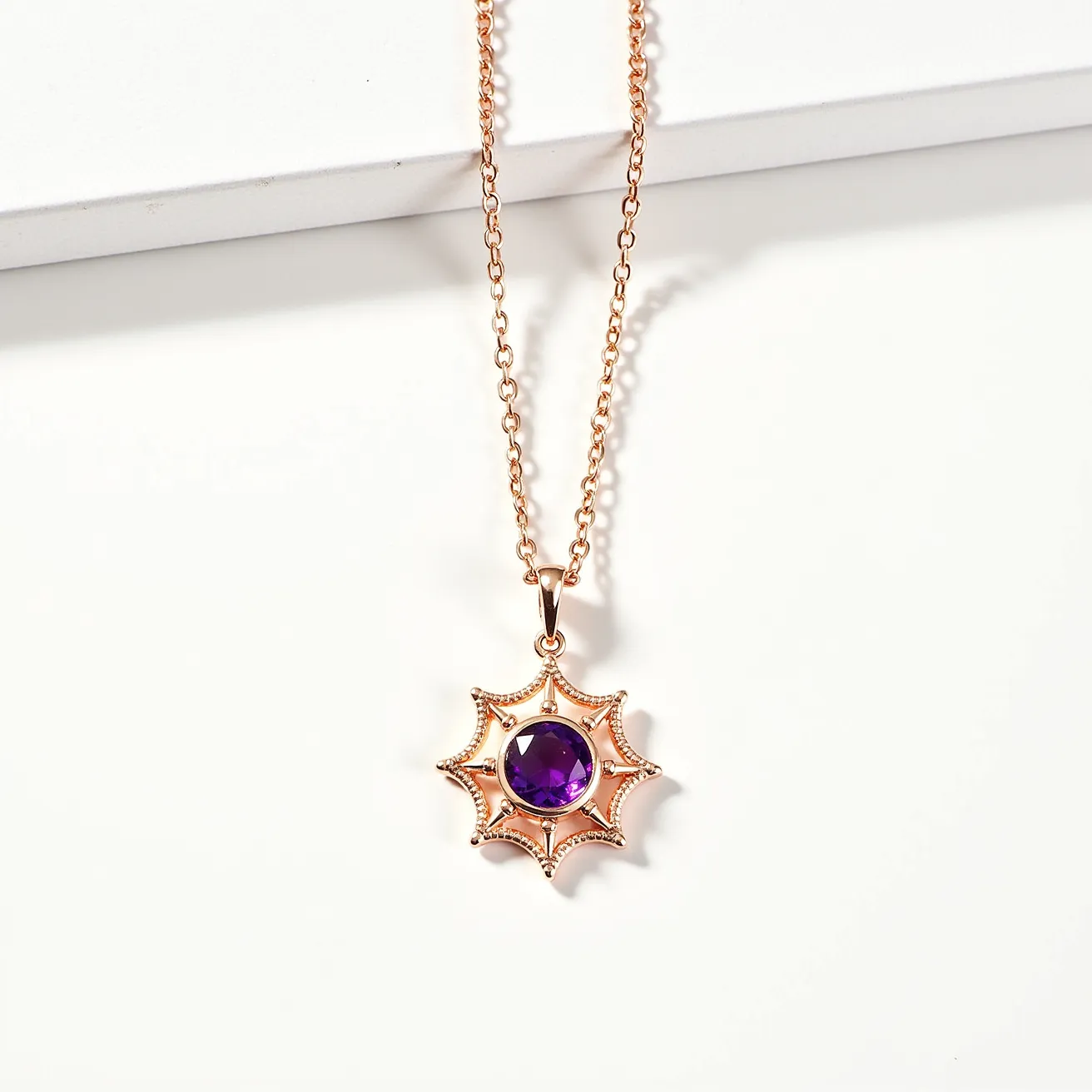 This pendant necklace features a captivating design with a round, faceted amethyst stone set in the center, radiating a vivid purple hue. The gemstone is securely held in place by a radial, starburst-like setting crafted from a gold-toned metal, highlighting its intricate openwork design. The pendant is suspended from a delicate chain, also in a matching gold tone, enhancing its elegant appearance. The necklace is attached with a simple, discreet clasp, ensuring both style and security when worn.