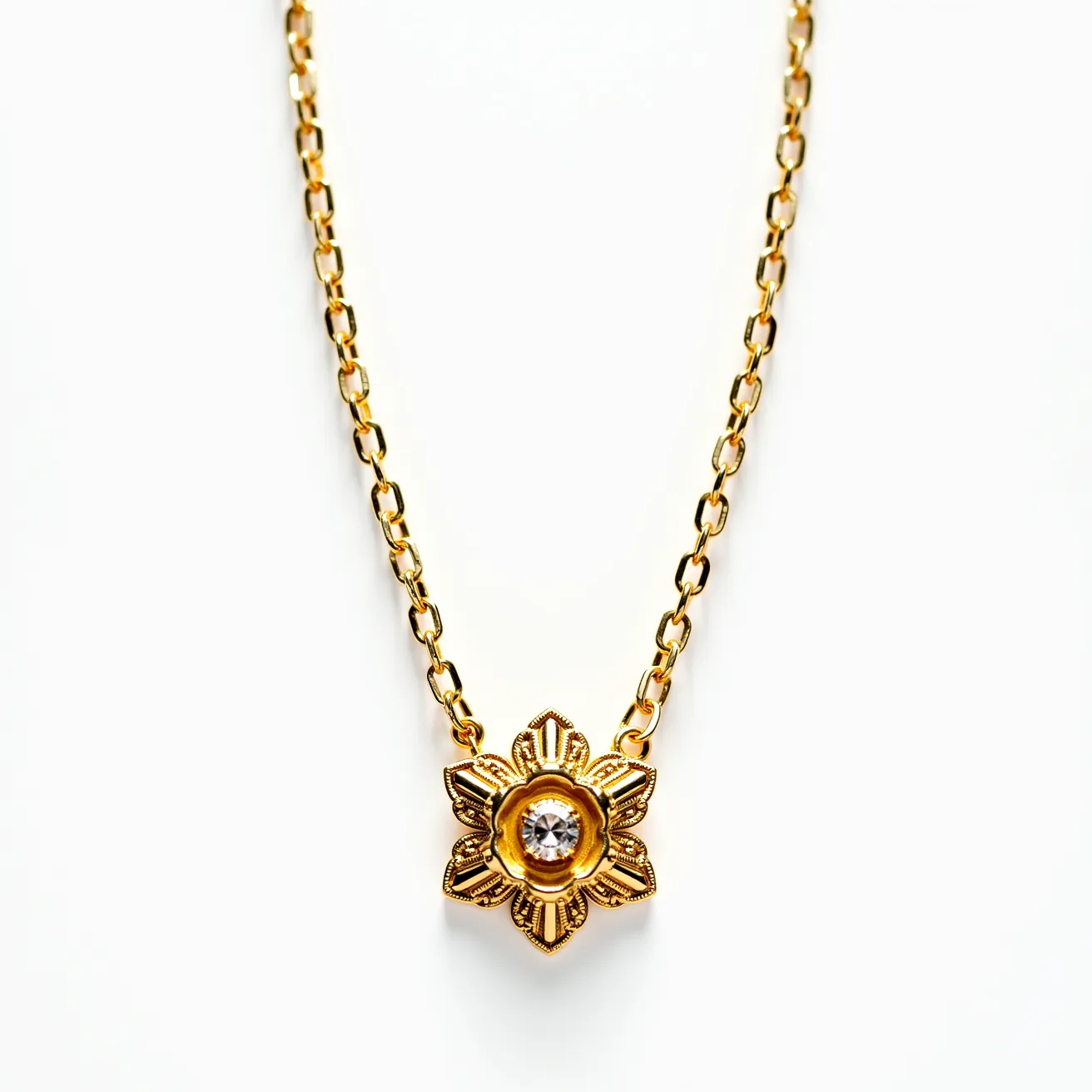 This pendant necklace features a gold-toned chain, linking towards a central floral pendant design. The pendant is crafted in a decorative floral pattern with intricate detailing and is centered around a round-cut stone, possibly a clear gem, securely set in a bezel setting. The chain is composed of oval links, offering a stylish yet classic look.