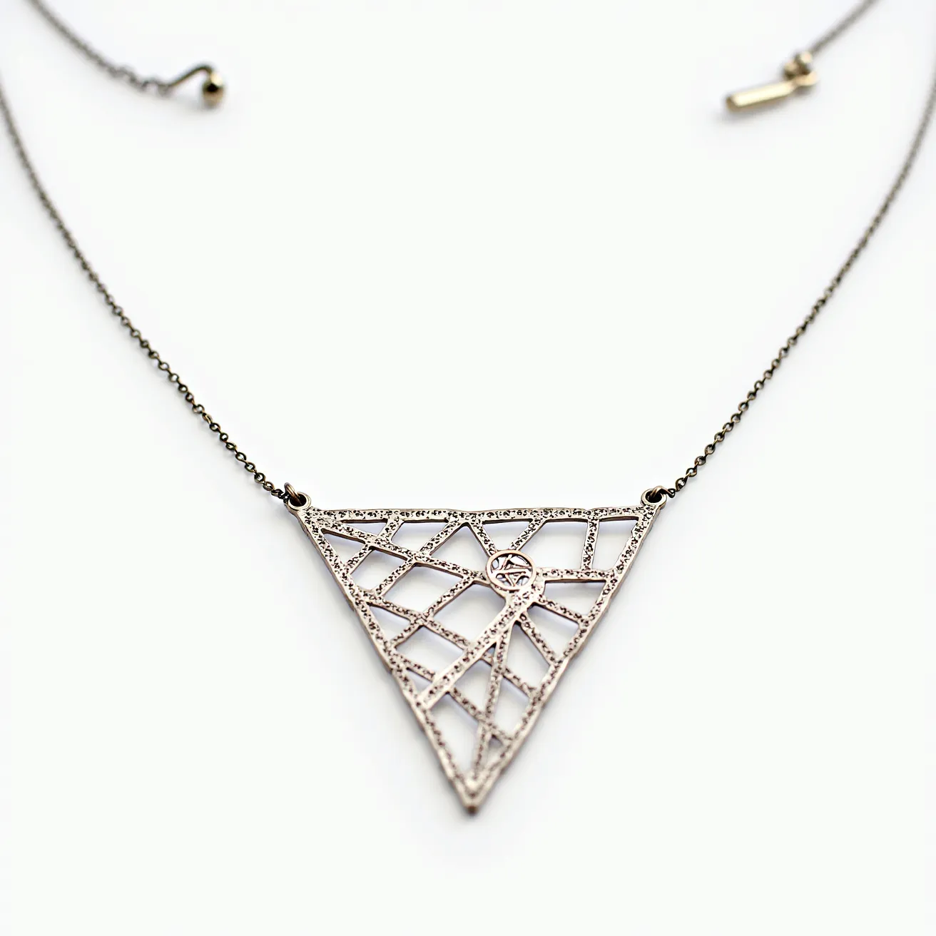 This pendant necklace features a triangular design crafted from metallic material, with intricate web-like patterns filling the interior. A single round gemstone, possibly a diamond, is accentuated at the center of the pendant, held in a bezel setting. The pendant is attached to a delicate chain, which appears to be made of a similar metal. The chain includes a simple clasp, likely a spring ring or lobster clasp, ensuring secure fastening and ease of wear.