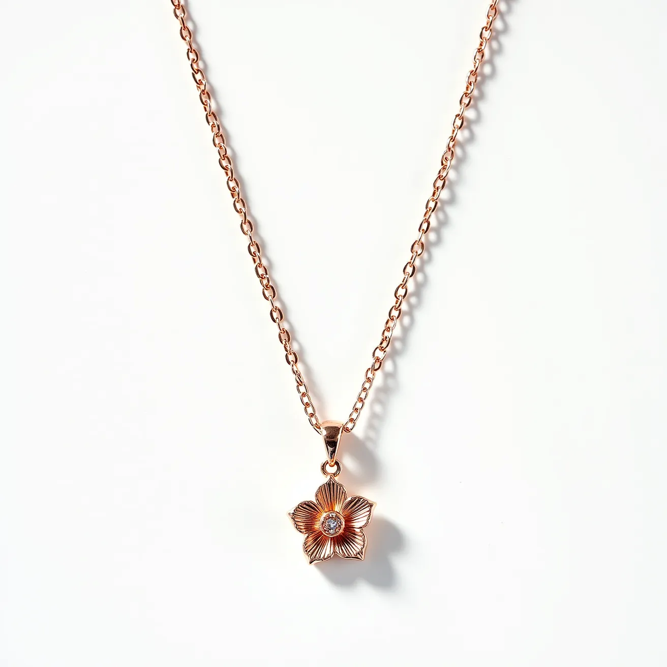 This pendant necklace features a delicate flower-shaped pendant crafted from rose gold-hued metal, adding a warm, elegant touch. The centerpiece of the pendant is a small, round gemstone set in the middle, which appears to be a diamond or a similar clear stone, cut to enhance its brilliance. The flower petals are intricately designed, emphasizing their natural form. The pendant is suspended from a matching rose gold-toned chain, completed with a simple and secure lobster clasp for attachment, ensuring easy wearing and removal.