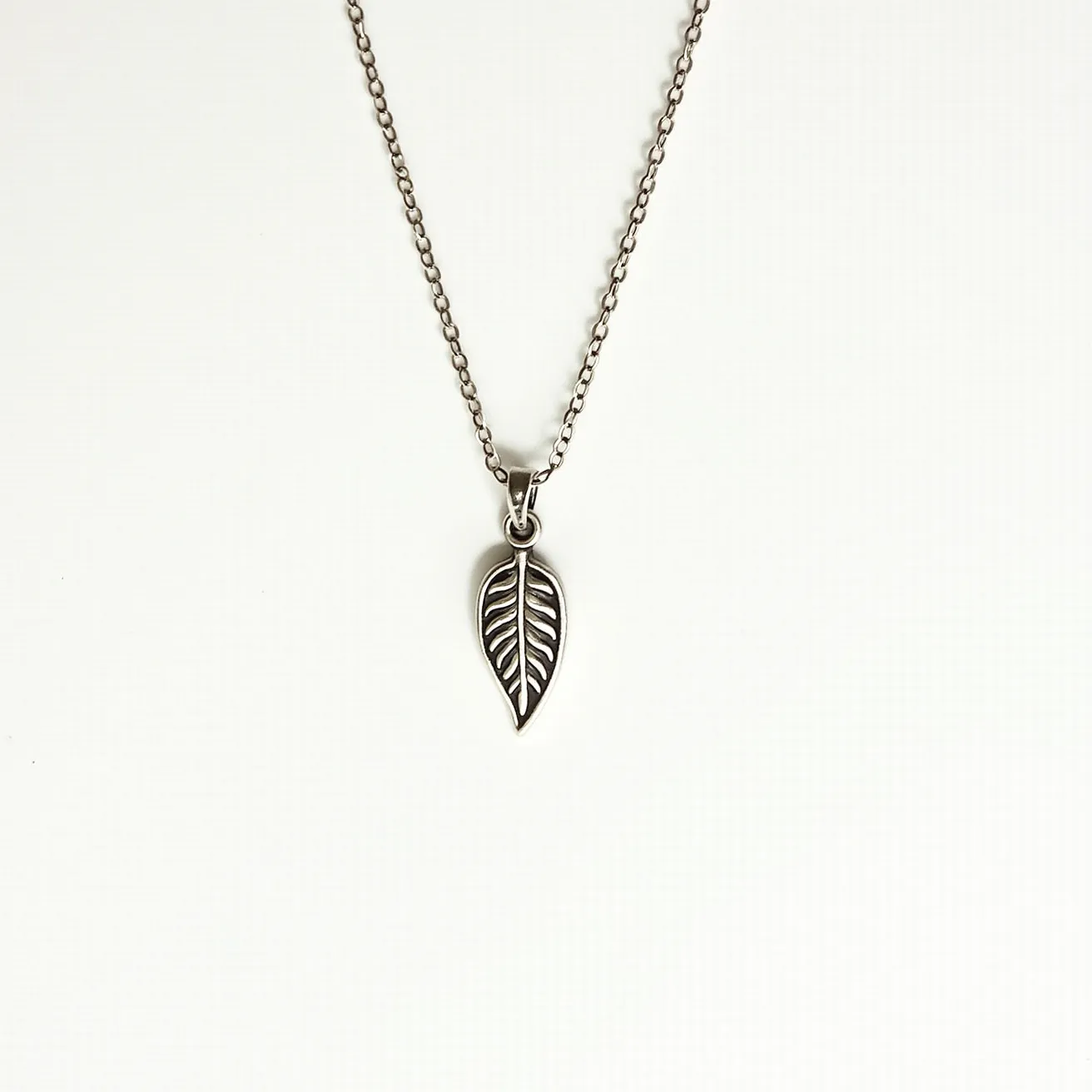 This pendant necklace features a delicate leaf-shaped pendant crafted from a silver-toned metal, showcasing intricate vein detailing that adds depth and texture to the design. The pendant is attached to a simple yet elegant chain through a small, secure bail, which allows for fluid movement and a harmonious fit. The chain is composed of interlocking oval links, providing a classic and timeless appeal. No gemstones are incorporated into the pendant, highlighting the metalwork as the focal point. The necklace likely fastens with a standard spring ring or similar clasp, ensuring ease of wear and security.