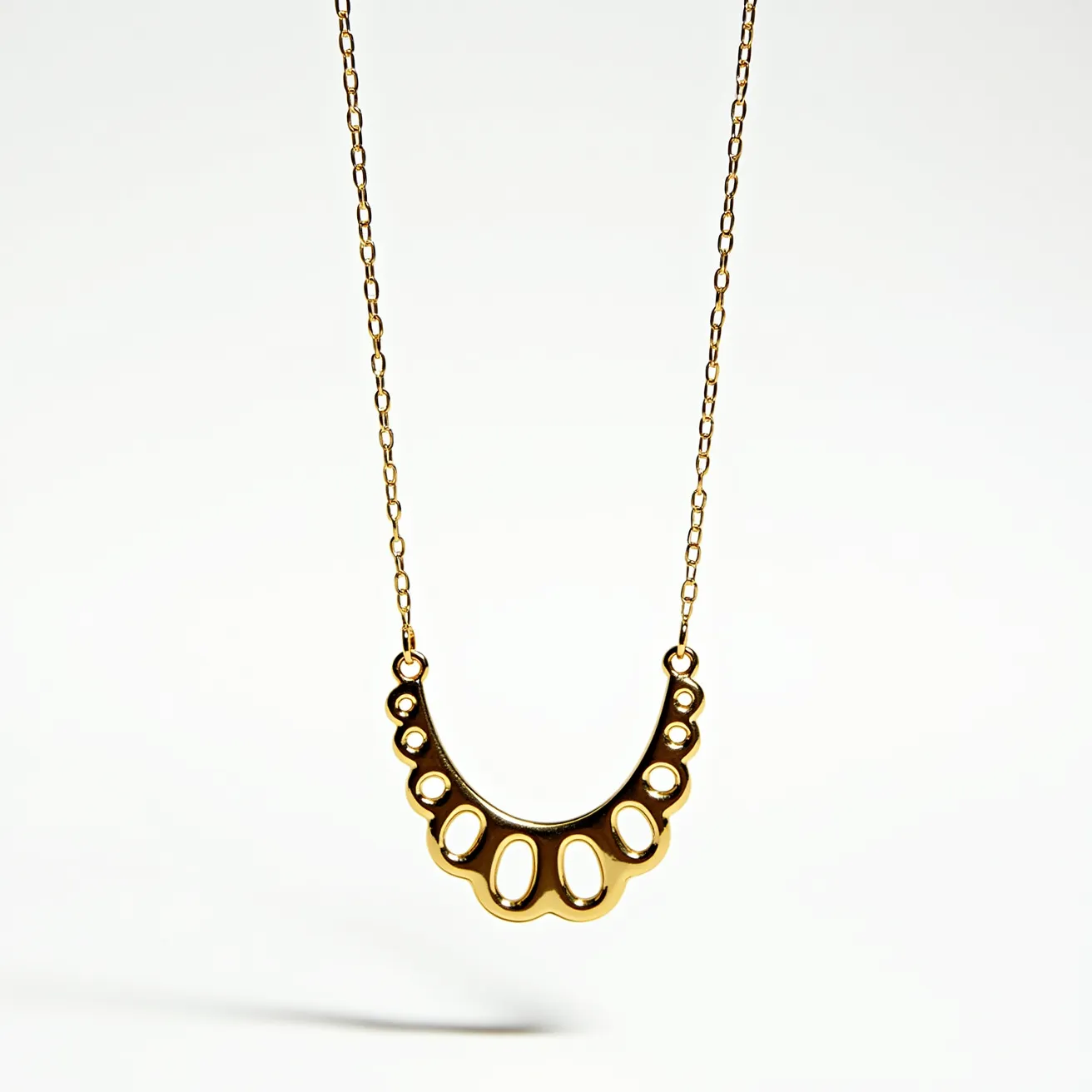 This pendant necklace features a delicate gold chain that supports a decorative pendant. The pendant is crafted in a scalloped design with openwork detailing, capturing a modern yet elegant aesthetic. The metal appears to be a polished gold, lending it a shiny and sleek finish. The necklace is joined by circular links connecting the pendant to the chain, providing a seamless attachment. The overall design combines simplicity with intricate detailing, making it a versatile accessory.