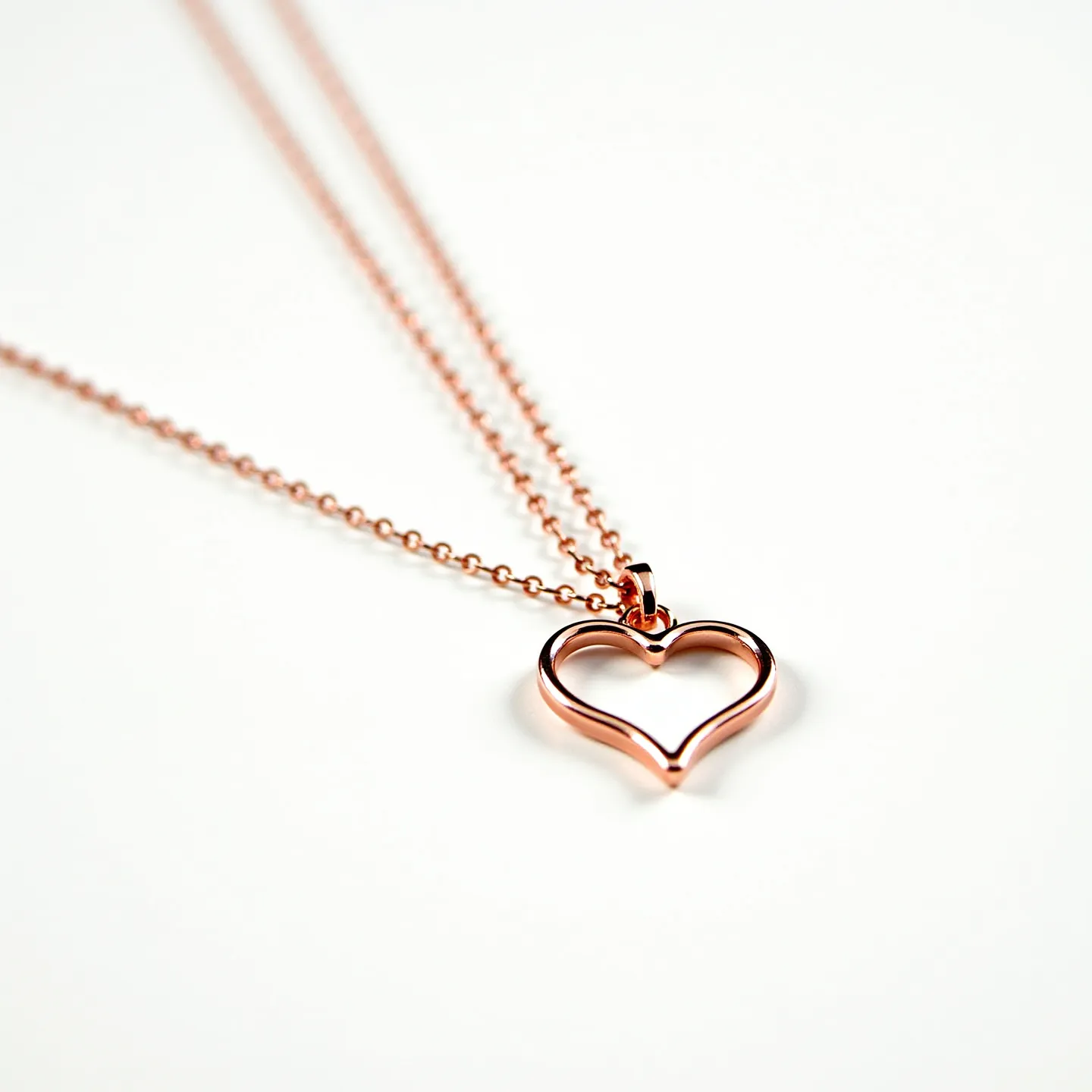 This pink heart necklace features a delicate chain crafted from a material with a rose gold finish, which complements the overall pink hue of the design. The pendant is shaped as an open heart, maintaining the same rose gold aesthetic as the chain, giving it a cohesive and elegant appearance. The necklace is likely designed without any additional gems or stones, and the heart pendant hangs gracefully from the chain. The attachment of the pendant is facilitated by a small loop, allowing it to slide freely along the chain. The necklace likely includes a clasp, typical of chain necklaces, to secure it in place when worn.