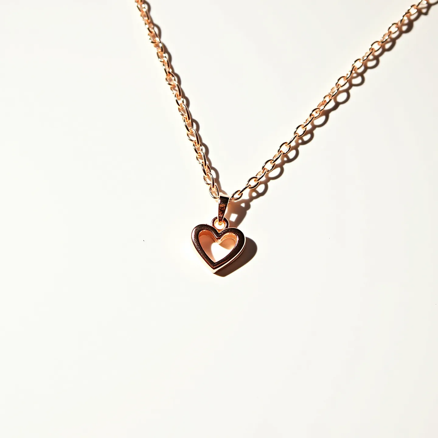 This pink heart necklace features a delicate chain crafted from a rose gold-toned metal, adding a subtle shine to the accessory. The pendant is a hollow heart shape, made from the same rose gold material, emphasizing its elegant design. The chain is constructed with oval links, giving it a classic appearance and ensuring durability. It is attached with a simple loop to the heart pendant, allowing for fluid movement. The clasp used is likely a standard spring ring or lobster clasp, common for securing lightweight necklaces comfortably and reliably.