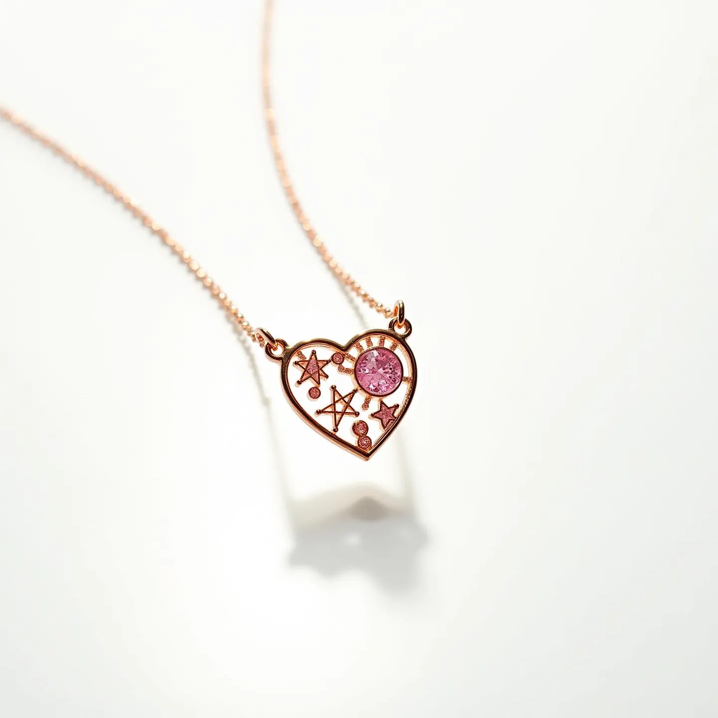 This pink heart necklace features an intricate design, characterized by a heart-shaped pendant made of rose gold-tone metal. Within the heart, there is a striking pink gemstone, likely a round-cut stone, set prominently with a bezel setting for security and style. The heart is adorned with star and planet motifs, adding a whimsical, celestial theme to the piece. The chain appears to be a delicate cable style, complementing the pendant's elegance. The necklace includes small attachment loops integrated into the design, ensuring the pendant hangs gracefully from the chain.