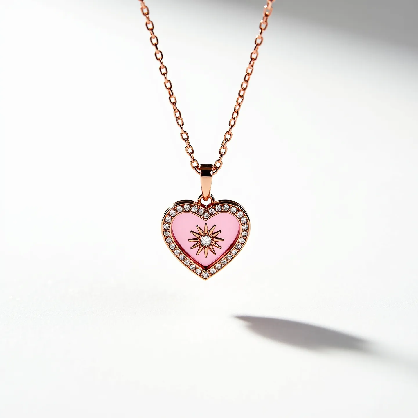 This pink heart necklace features a heart-shaped pendant with a vibrant pink enamel center. It is adorned with a starburst design at the center, which appears to house a small white gemstone or diamond in a prong setting. The outer edge of the heart is encrusted with a series of small, round-cut white stones, likely diamonds or cubic zirconia, set in a pavé style. The pendant is attached to a delicate chain with a rose gold hue, complementing the pendant's warm tones. The necklace is secured with a standard clasp, which ensures ease of wear and removal, enhancing its elegance and charm.