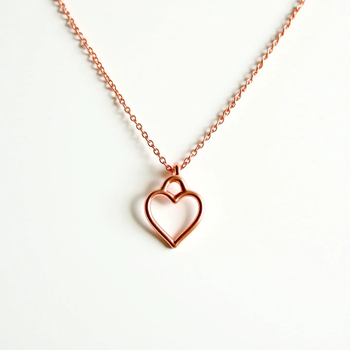 This pink heart necklace features a delicate, open-heart pendant crafted from a polished metal, possibly rose gold or copper, giving it a warm pink hue. The design is simple, with smooth, curved lines forming the heart shape, attached to a fine chain that complements the pendant’s color and style. The chain consists of small, round links, creating a subtle yet elegant look. The necklace is likely secured with a standard spring ring or lobster clasp, providing an easy and reliable attachment. Overall, the design exudes a modern and minimalist aesthetic.