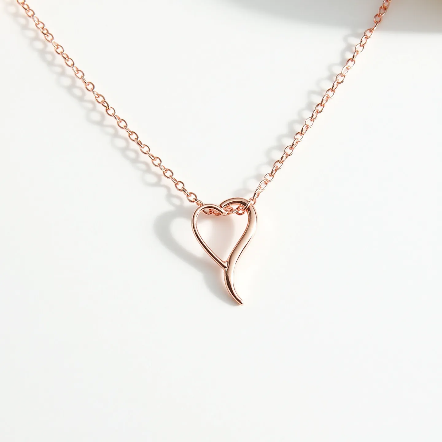 This pink heart necklace features a delicate chain made of rose gold metal, giving it a warm, rosy hue. The pendant is designed as an abstract heart shape, crafted from the same rose gold material, which adds a sleek and modern touch. It does not include any additional gemstones. The necklace likely employs a simple clasp mechanism, typical of chain necklaces, to ensure secure wear. The overall design is minimalistic and elegant, making it suitable for various occasions.