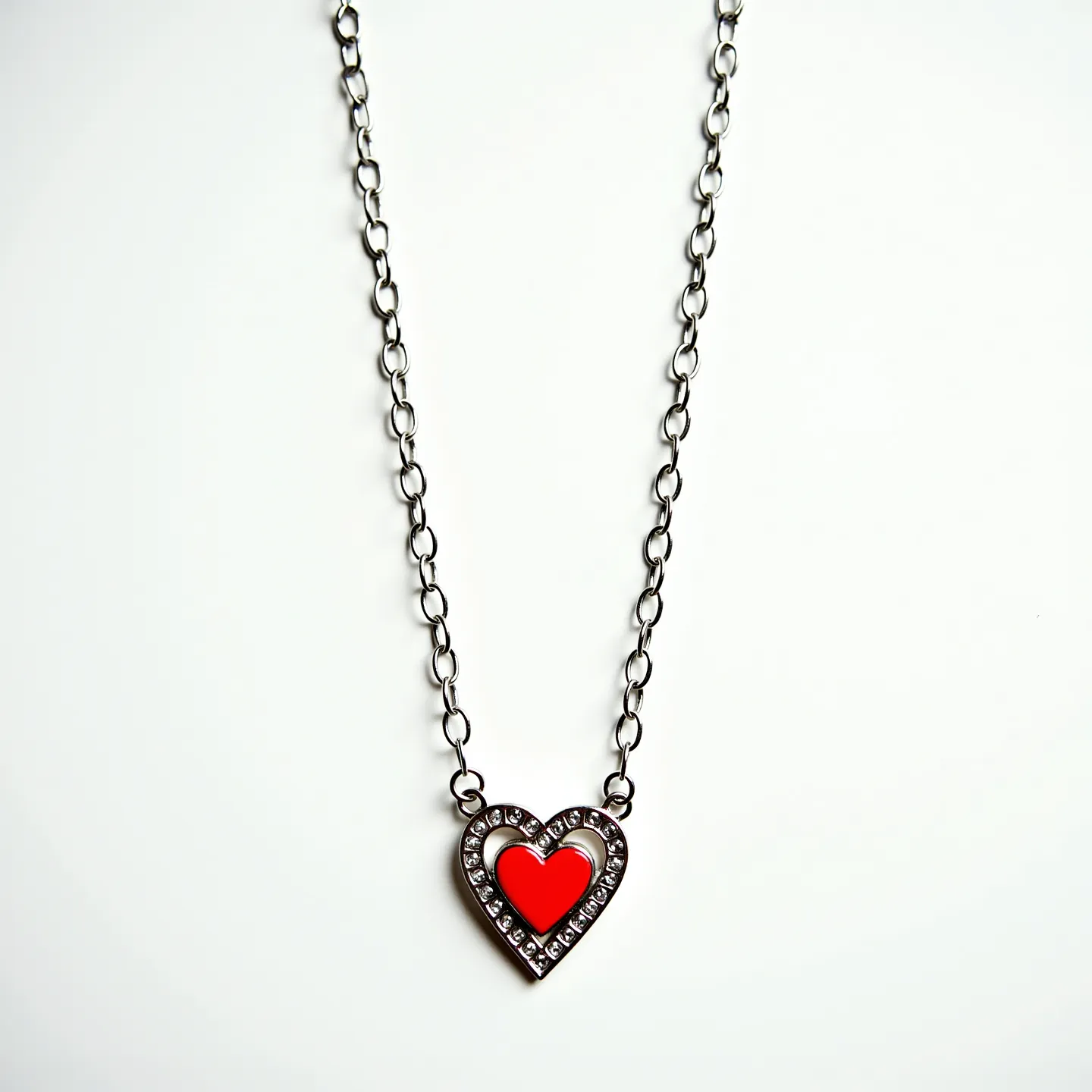 This red necklace features a striking heart-shaped pendant with a vivid red center, surrounded by a series of clear stones set in an outer heart-shaped metal frame. The stones appear to be faceted, enhancing their sparkle and adding a delicate contrast to the bold red centerpiece. The pendant is suspended from a metal chain composed of interlocking oval links, creating a simple yet elegant design. The necklace is likely closed with a standard clasp, though it is not detailed in this view, providing a secure and easy attachment.