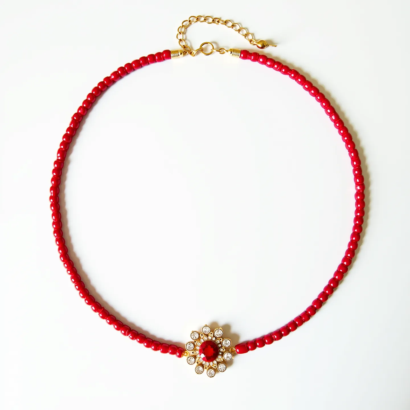 This red necklace features a series of round red beads meticulously threaded along a single strand, creating a vibrant and cohesive design. At the center, there is a striking floral pendant with a red gemstone at its heart, surrounded by small, clear stones set in a classic prong setting, giving it a sparkling finish. The necklace is equipped with a gold-toned chain and a lobster clasp, allowing for adjustable length and secure closure. The combination of the bold red beads and shimmering center accentuates an eye-catching and elegant appearance.