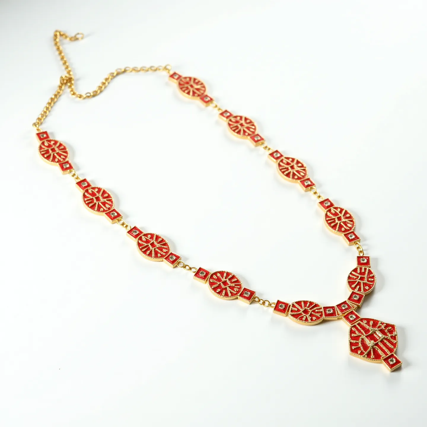 This red necklace features a series of circular and square elements, each adorned with intricate red enamel or inlay work, creating an ornate pattern. The circular components appear to have a design reminiscent of a sunburst, while the smaller square connectors provide a symmetrical transition between the larger pieces. The central feature of the necklace is a larger pendant with a similar pattern, enhancing its decorative appearance. The necklace is interlinked with gold-toned metal, contributing to a cohesive and polished look. The clasp is a simple chain link style, allowing for adjustable length and ease of wear.