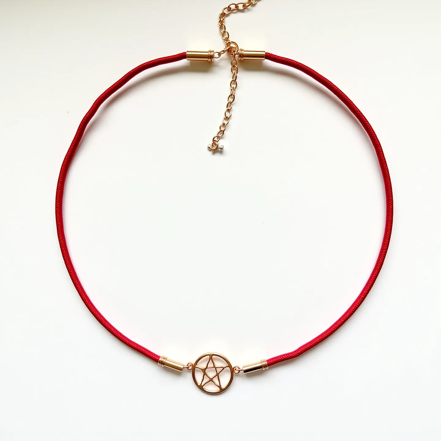 This red necklace features a vibrant red cord that seamlessly integrates with a central gold-toned metal pendant in the shape of a pentagram enclosed in a circle. The pendant is a minimalist, open-frame design, providing a focal point on the necklace. The clasp mechanism consists of a gold-toned adjustable chain with a lobster claw clasp, allowing for variations in length. The cord is attached to the chain by cylindrical gold-toned connectors that complement the pendant, creating a cohesive design. No gemstones are present, emphasizing the simplicity and elegance of the piece.