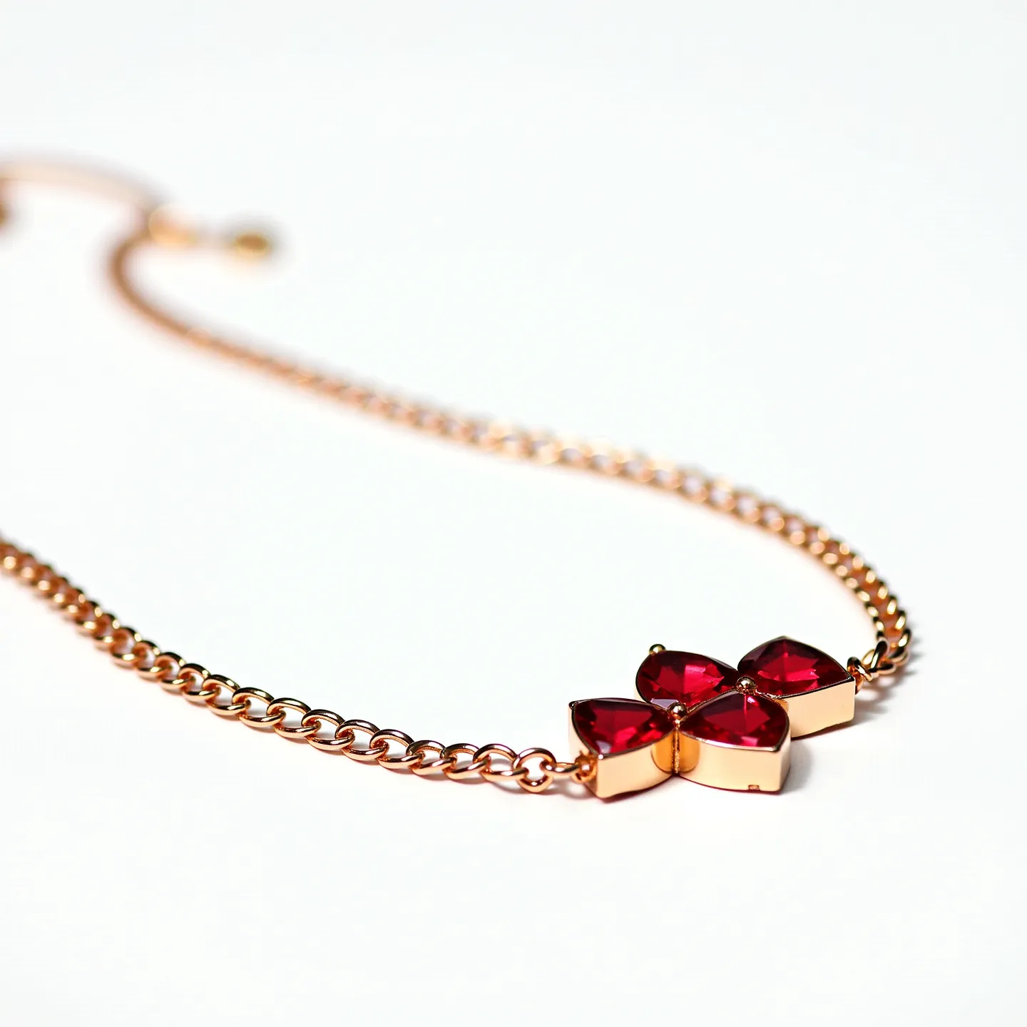 This red necklace features a gold-toned chain with a centerpiece of four red gemstones arranged in a floral motif. The gemstones are pear-shaped, displaying a vibrant red hue, and are securely set in a unique pronged setting that accentuates their shape. The chain is designed with interlocking links, providing a smooth and elegant drape around the neck. At the back, the necklace is equipped with a small, gold-toned sliding bead clasp, allowing for adjustable sizing and secure fastening. The combination of the rich red stones and the gold chain creates a striking and sophisticated piece of jewelry.