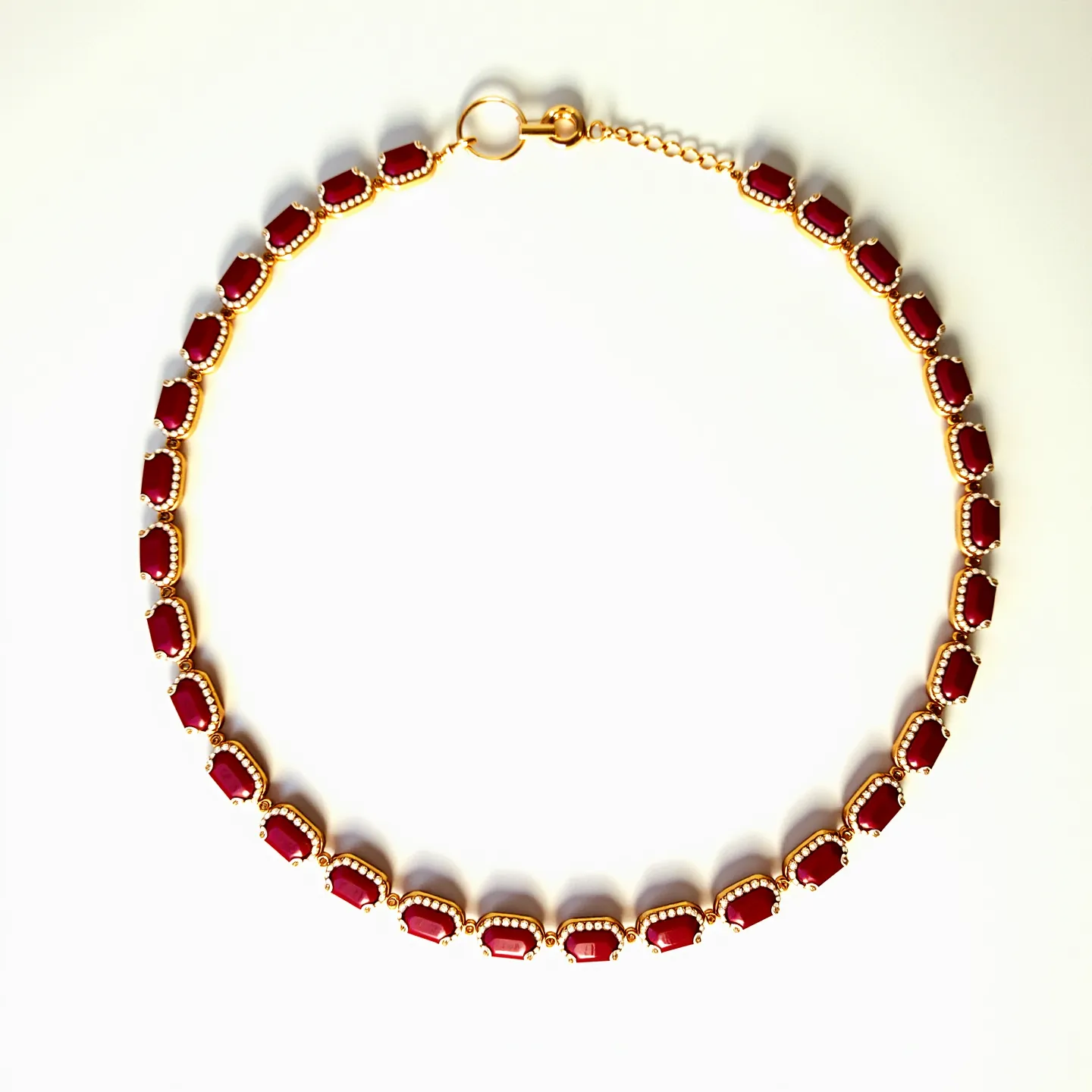 This red necklace features a series of rectangular, polished red stones that are uniformly set in a classic prong setting. Each stone is bordered by a delicate gold or gold-colored trim, enhancing their rich hue. The stones are connected by small, round accents that resemble beads, adding a subtle texture and visual interest. The necklace is secured with a lobster clasp, which is attached to a short extension chain, allowing for adjustable length. The overall design is elegant and sophisticated, with a harmonious blend of bold color and refined metallic elements.