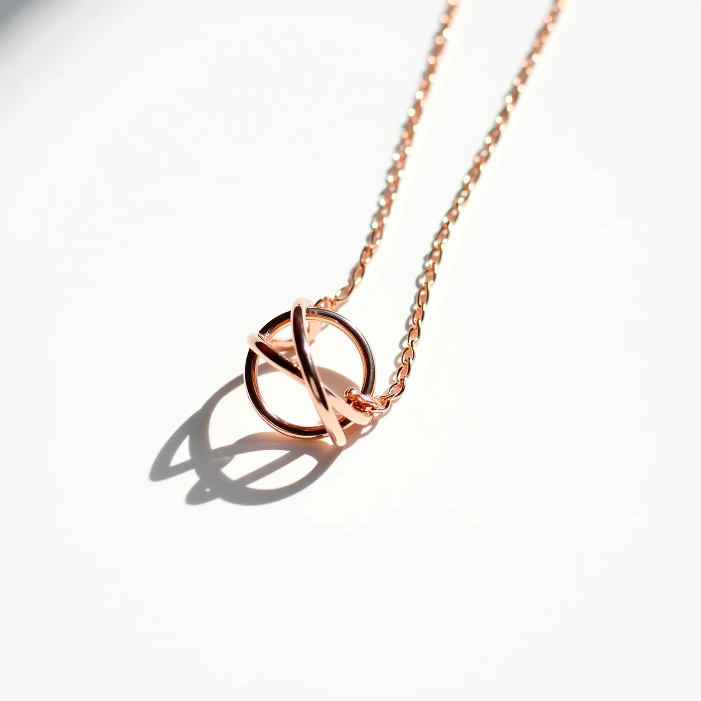 This ring necklace features a delicate chain crafted from a rose gold-colored metal, giving it a warm and elegant appearance. At the center, a small ring serves as the pendant, intertwined with another slender band creating an intersecting loop design. The necklace highlights the sleek, polished finish of the metal, enhancing its refined look. It is likely secured with a classic lobster clasp or similar fastening mechanism, ensuring a secure and comfortable fit around the neck. The absence of gemstones or additional embellishments emphasizes the minimalist and modern aesthetic of the necklace.