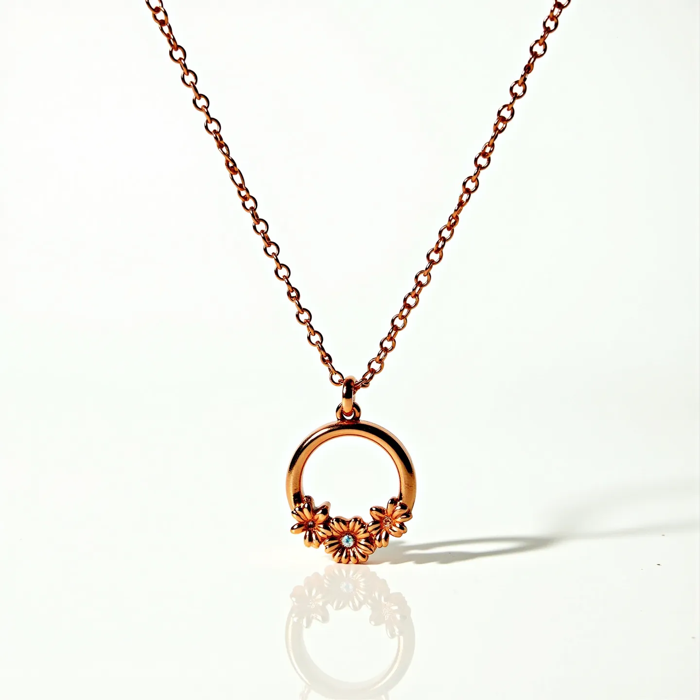 This ring necklace features a delicate rose gold chain that supports a circular pendant adorned with floral motifs. The pendant is intricately designed with three daisy-like flowers, each enhancing the elegant design. At the center of each flower, a small, clear gemstone is set, adding a hint of sparkle to the piece. The chain appears to have a simple, understated clasp that complements the overall aesthetic, providing both functionality and style to the necklace.