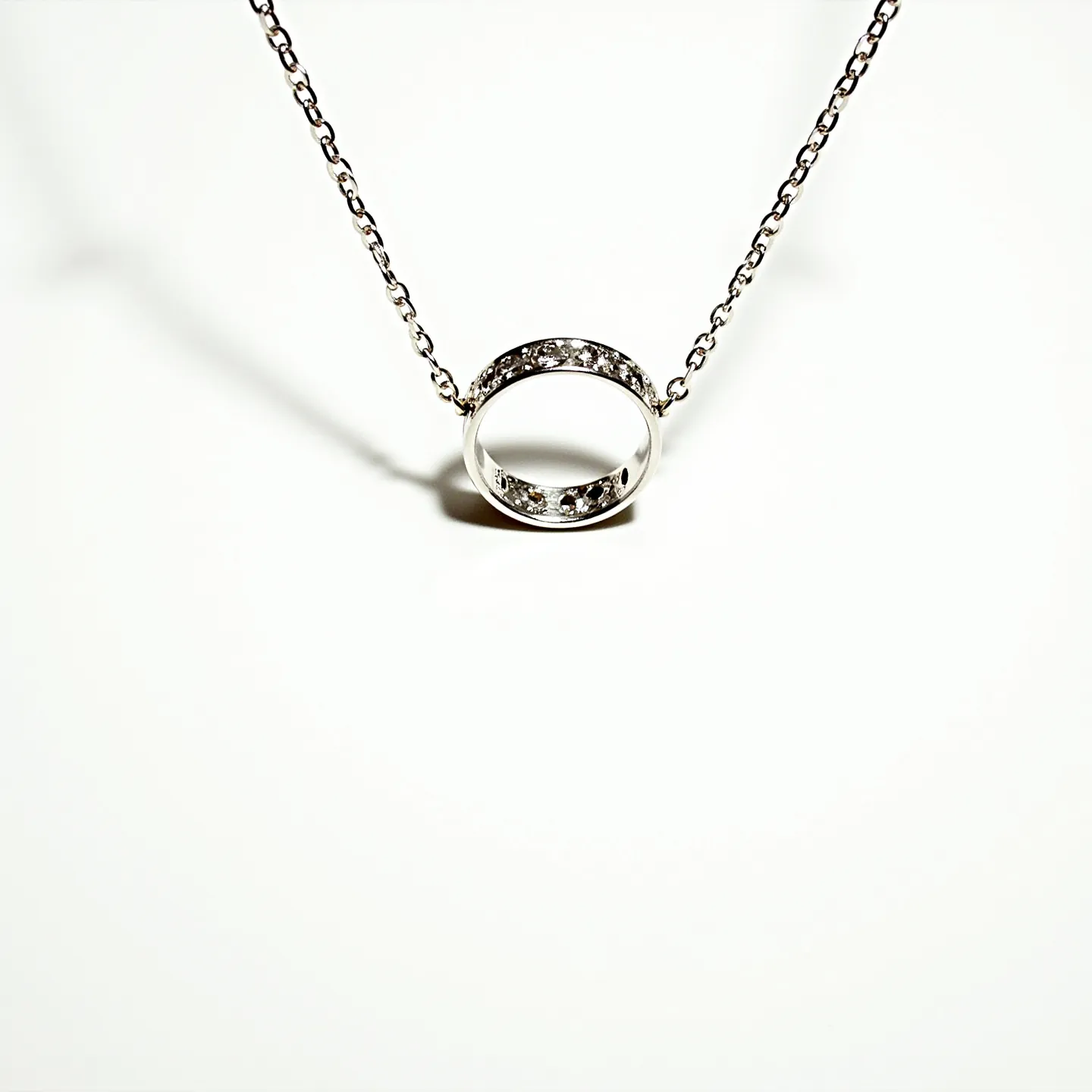 This ring necklace features a smooth, circular pendant with a polished finish, likely made of silver or white gold. It is adorned with several small, brilliant-cut stones, possibly diamonds, set in a channel setting that adds a sophisticated sparkle to the piece. The chain is a delicate cable link, likely matching the metal of the ring pendant, which gives the necklace a cohesive and elegant appearance. A simple yet secure jump ring attachment integrates the pendant seamlessly into the chain, offering a classic and timeless design suitable for various occasions.